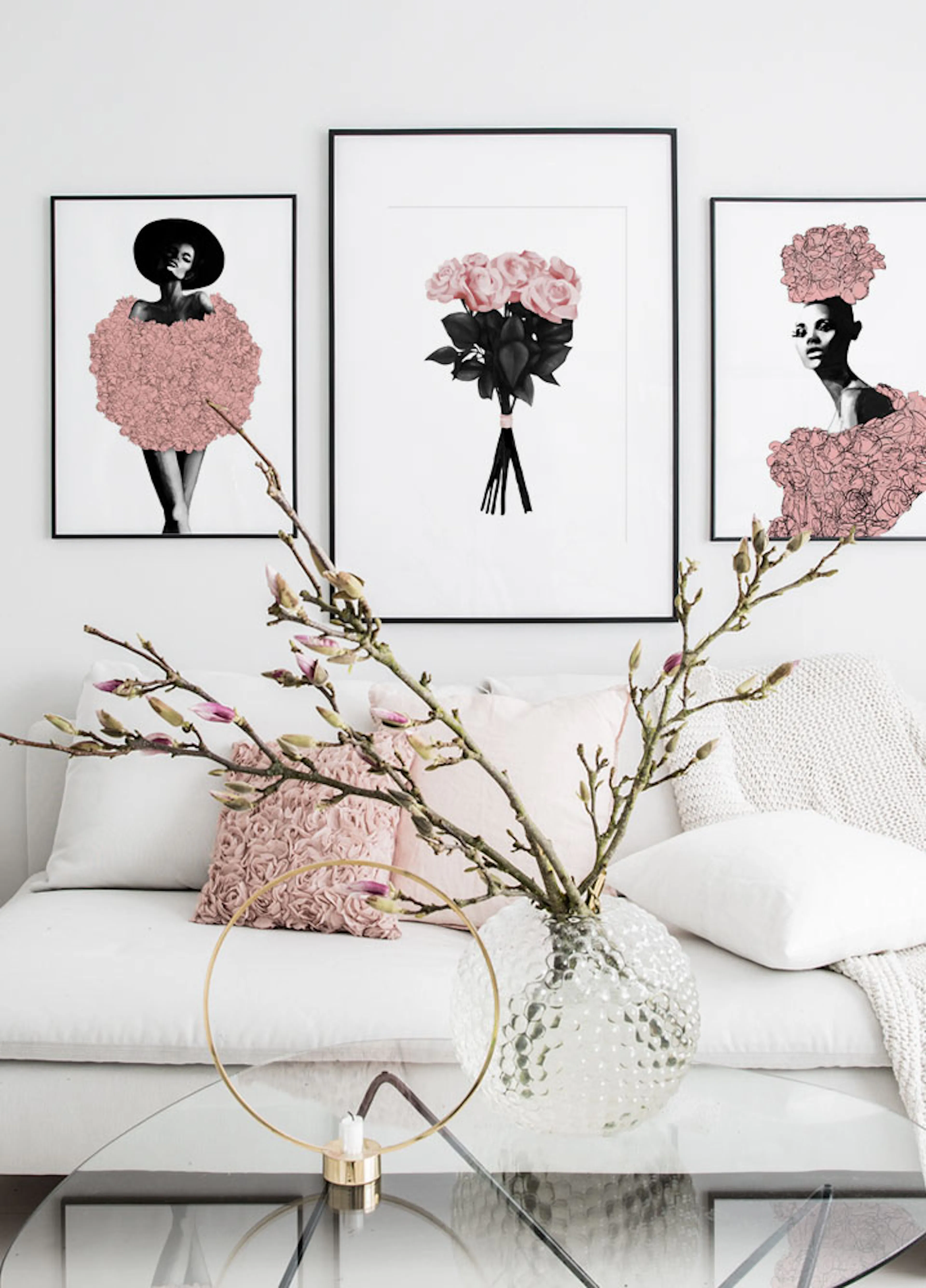 Three fashion posters with black and white figures and pink floral accents, hanging above a white sofa with pink cushions.