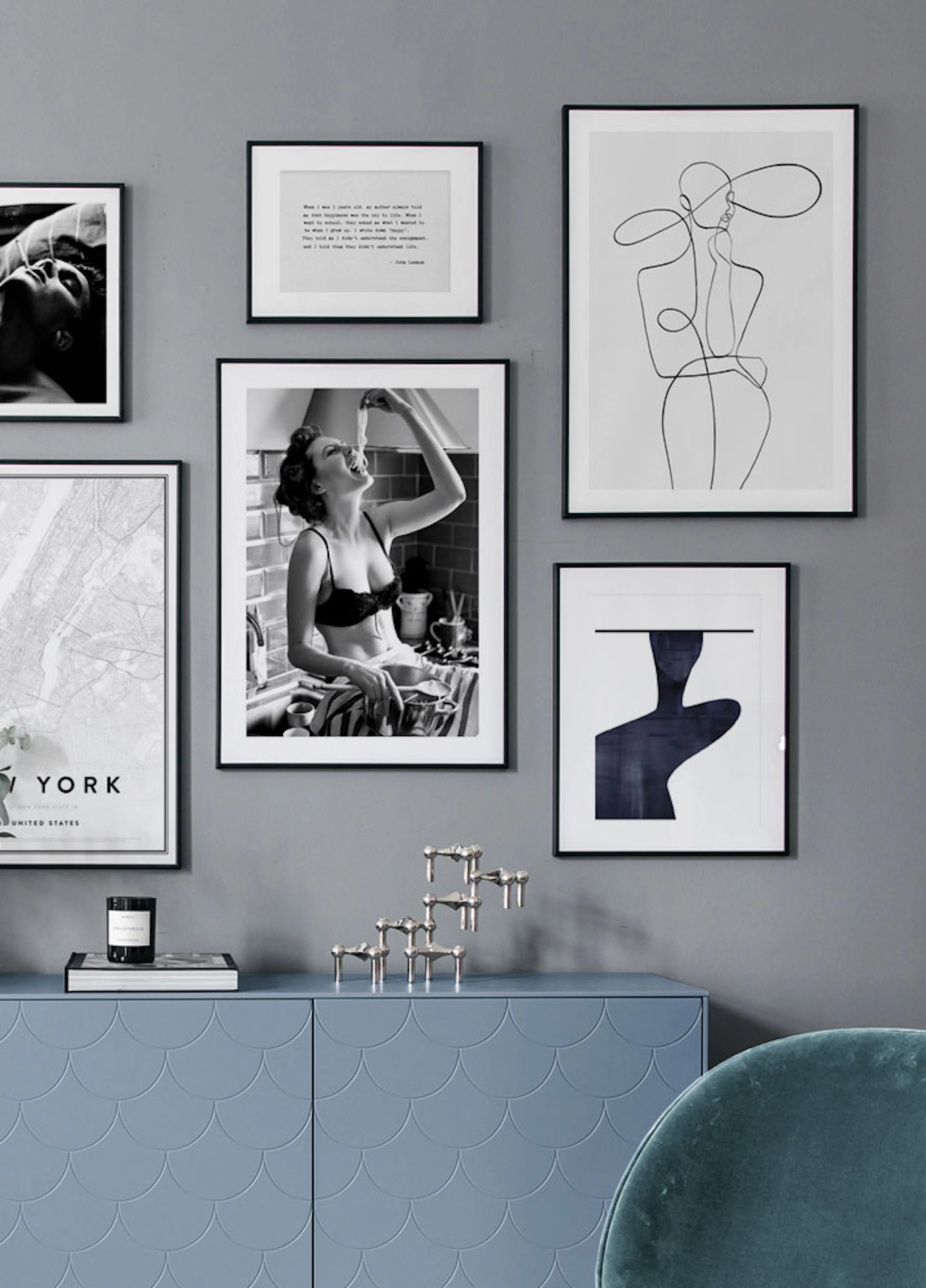 A gallery wall with black and white posters, including a woman eating pasta and a line art figure, displayed above a blue cabine