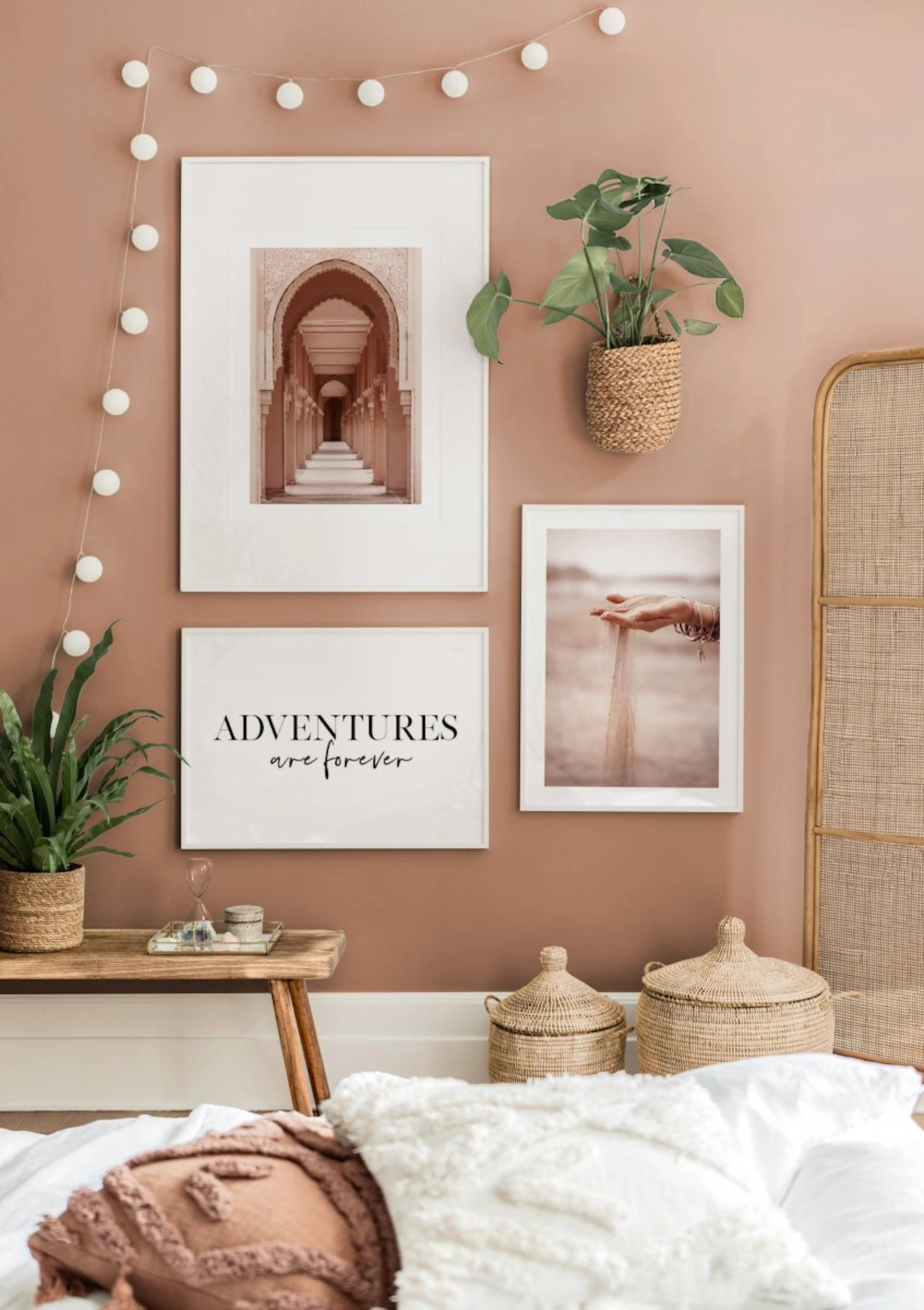 A gallery wall with three posters on a terracotta wall, including a desert archway, sand falling from hands, and ADVENTURES are 