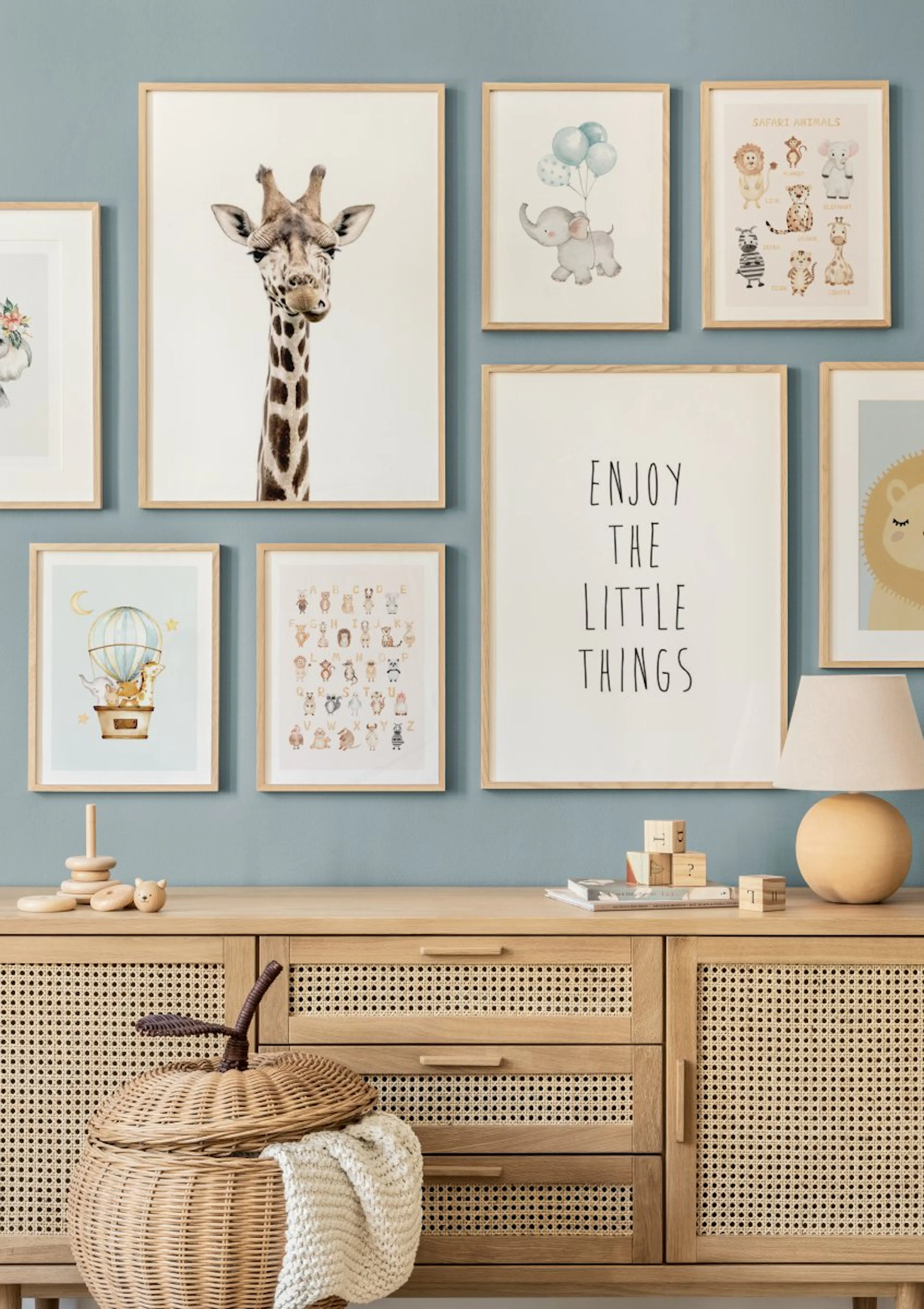 A gallery wall of nursery posters featuring a giraffe, elephant, and alphabet animals, displayed above a wooden sideboard with a