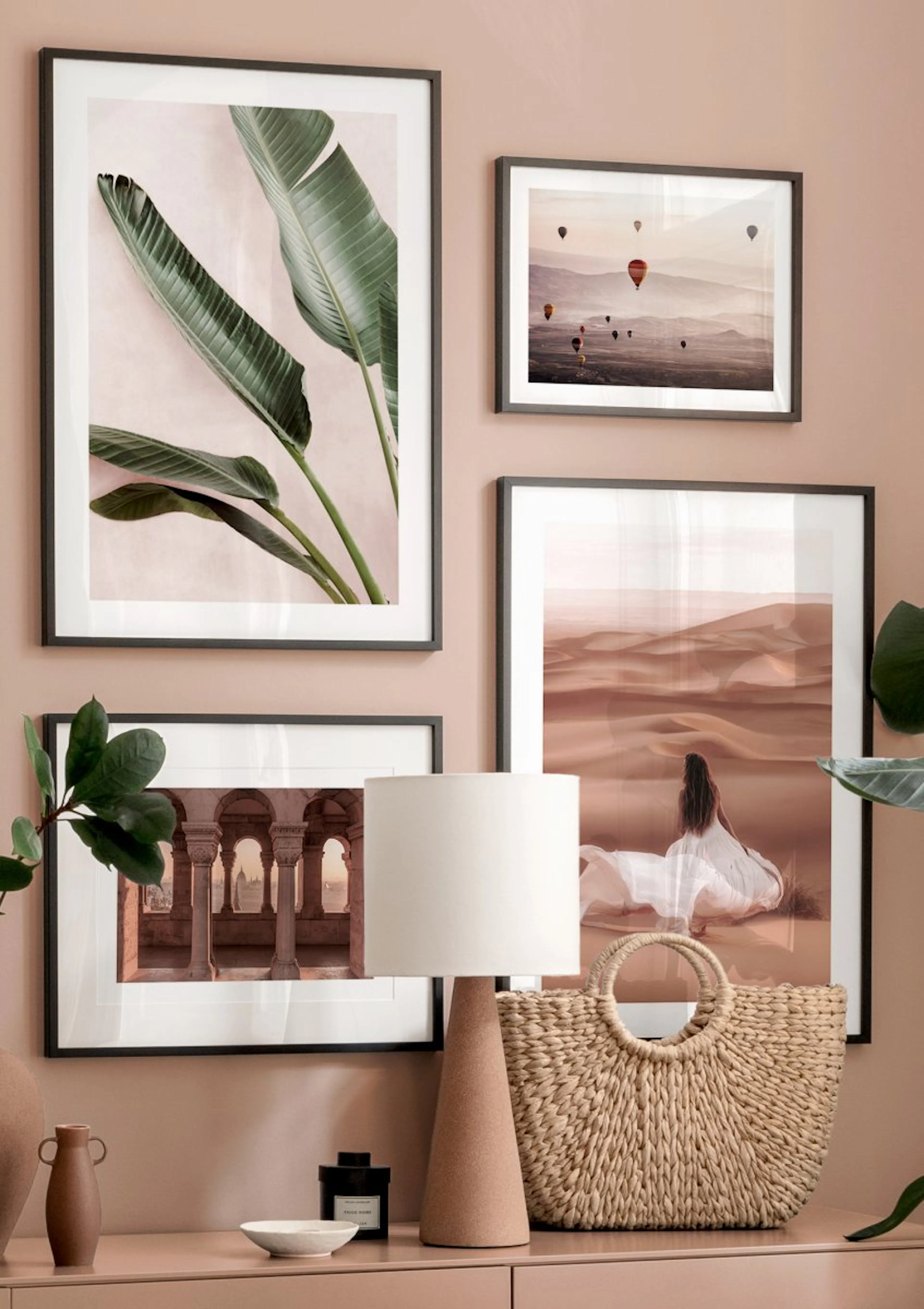 A gallery wall with four posters in a room with light peach walls and a wooden dresser. The posters feature a banana leaf, hot a