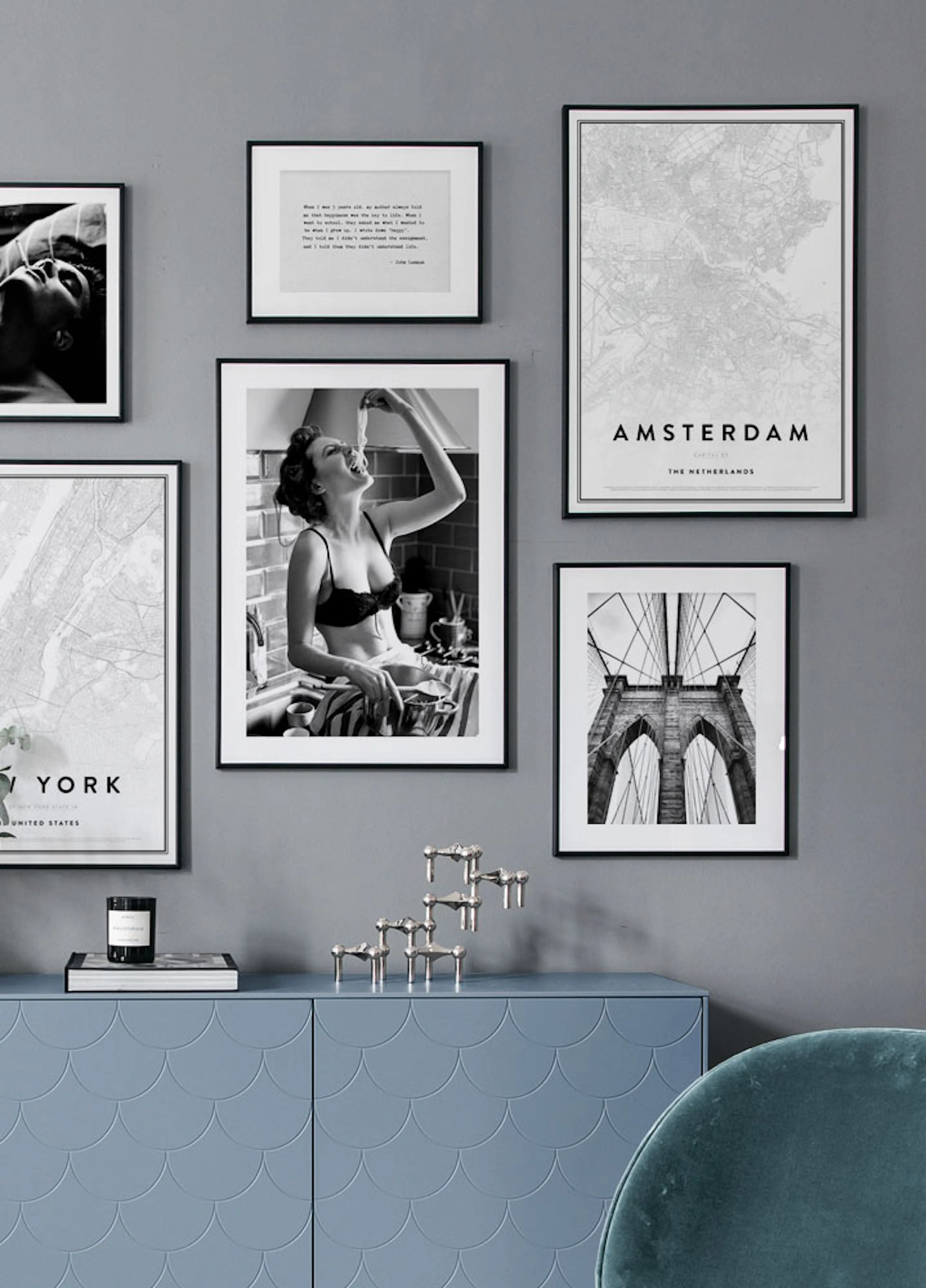 Eine Bilderwand mit Postern an einer grauen Wand, darunter ein hellblaues Sideboard mit Deko.