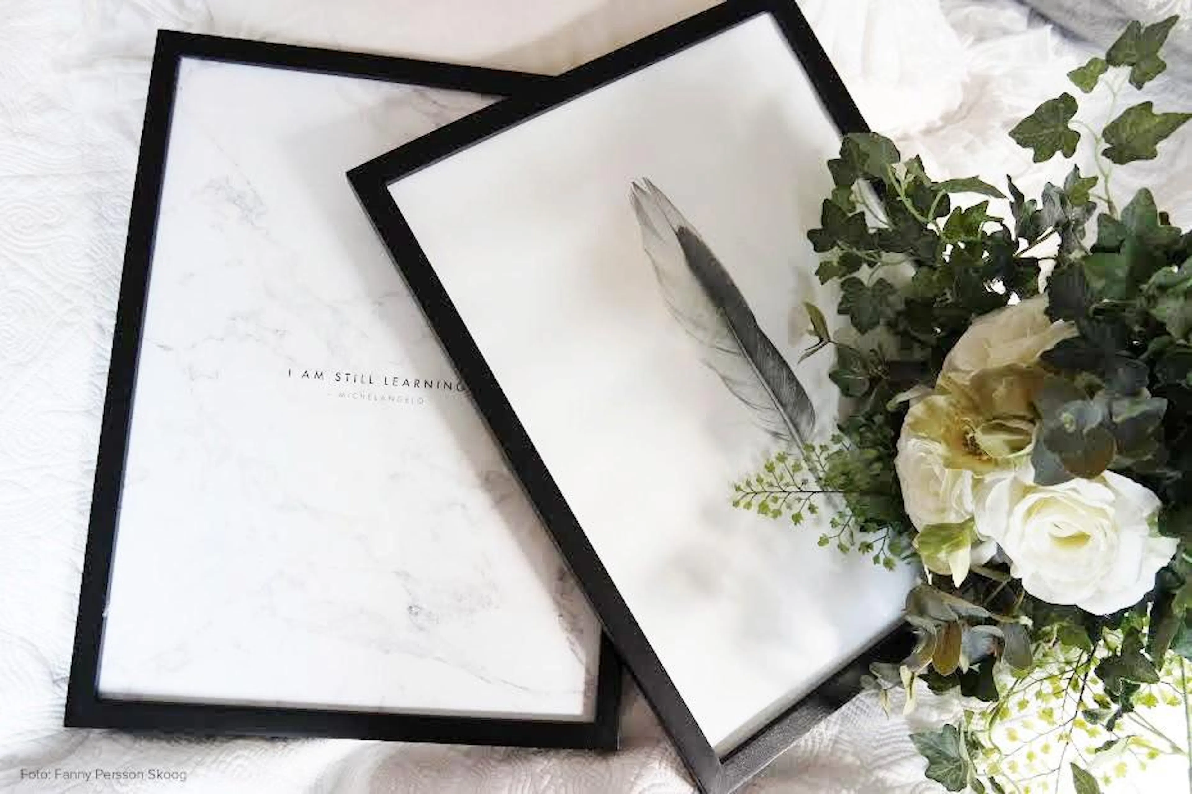 Dos pósters sobre una cama blanca, uno con una pluma y follaje, y otro con textura de mármol y la frase I AM STILL LEARNING.