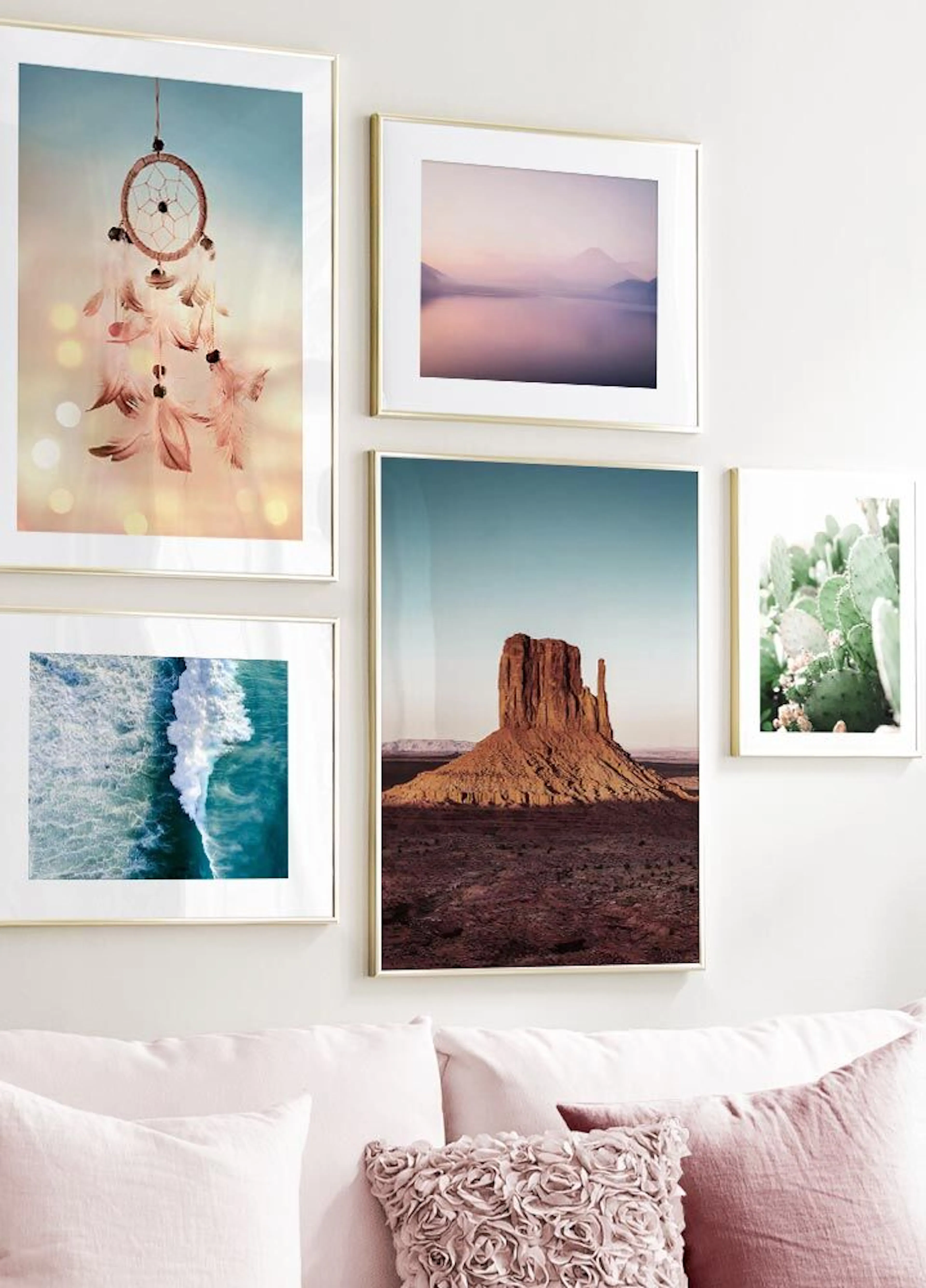 A gallery wall of posters above a pink sofa, featuring a dreamcatcher, desert formations, ocean waves, a lake, and a cactus.