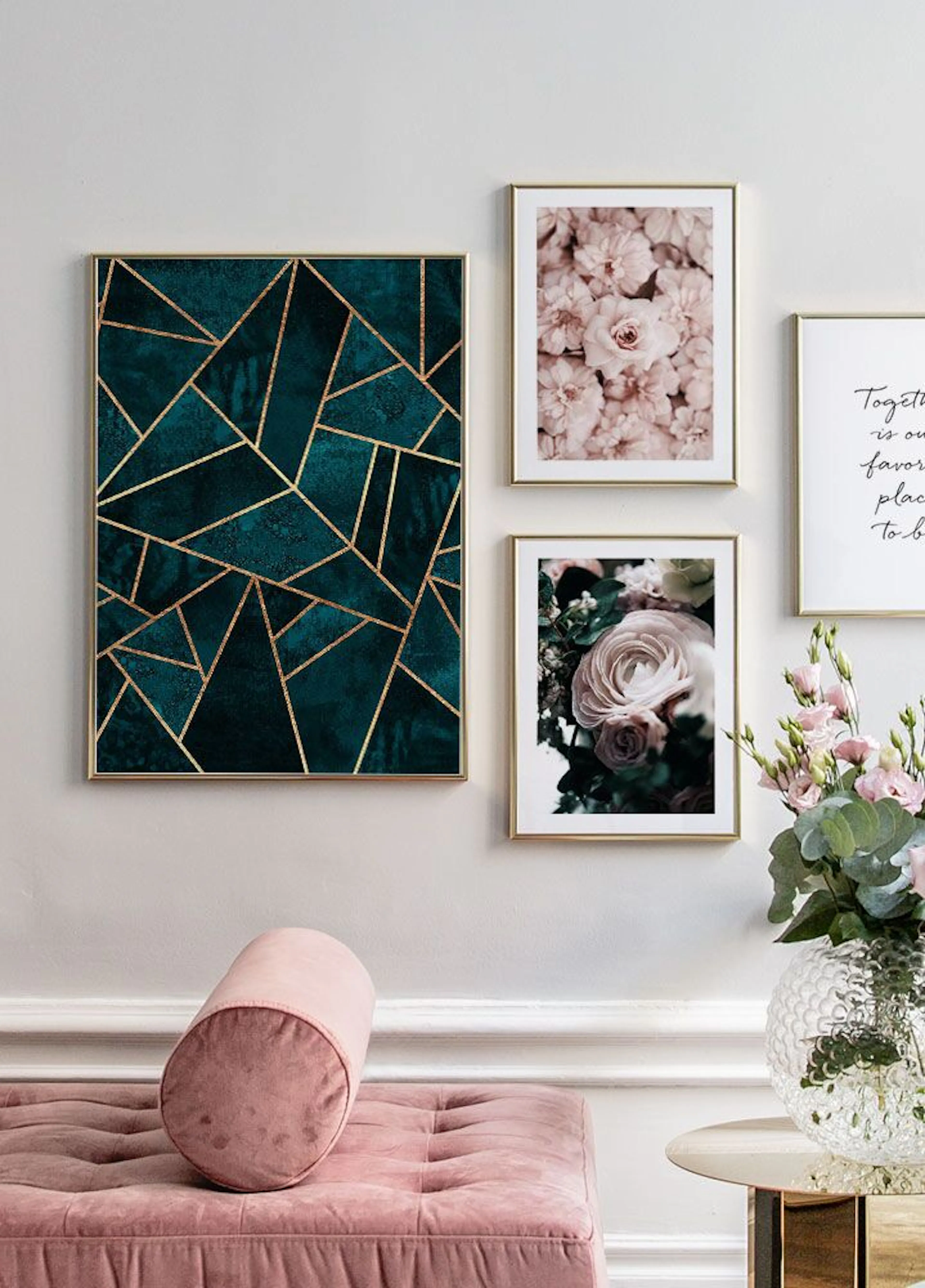 Plakát se smaragdově zelenými geometrickými tvary a zlatými liniemi, visící nad růžovou sedačkou v moderním interiéru.
