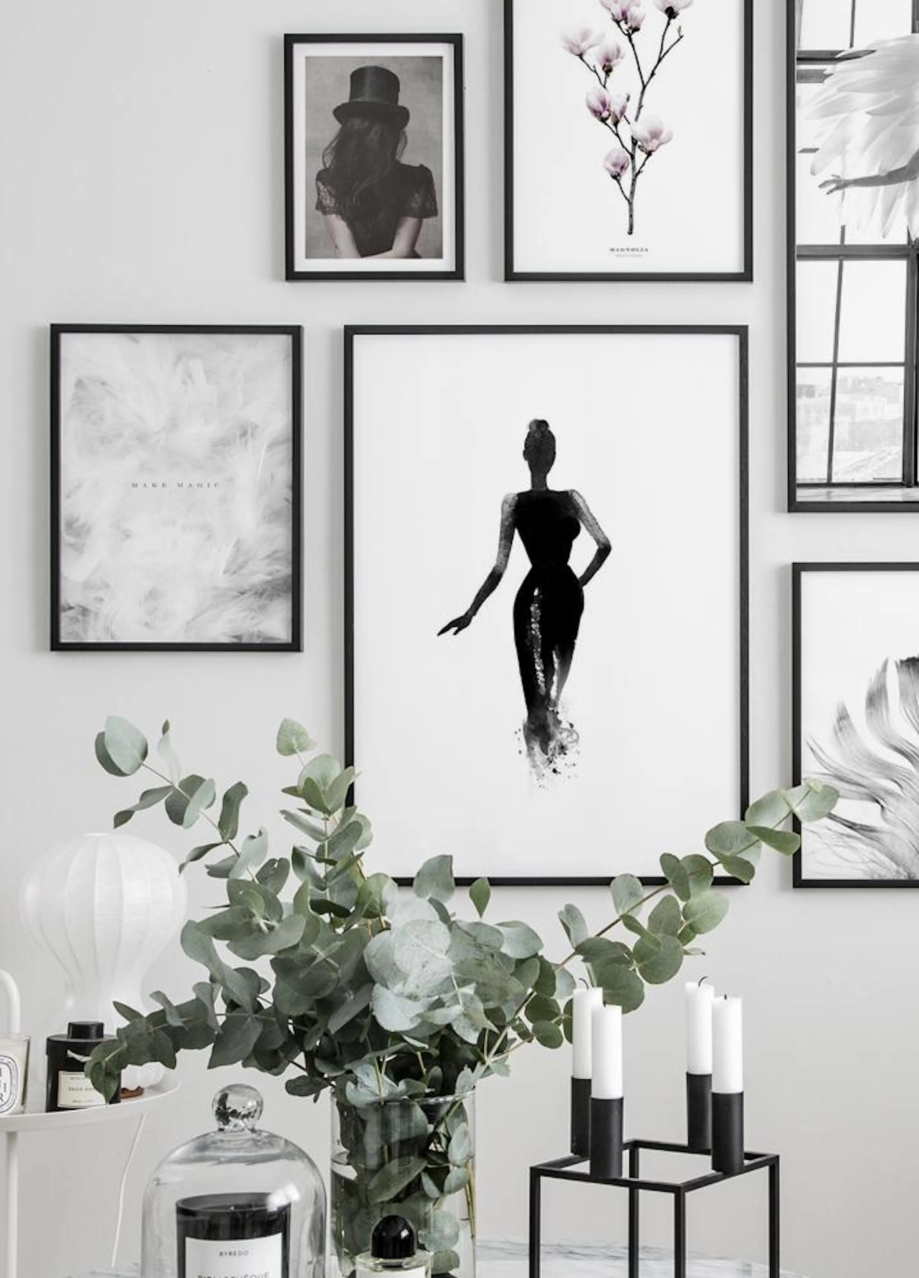Monochromatic poster of a silhouette of a woman in a dress, part of a gallery wall above a eucalyptus plant.