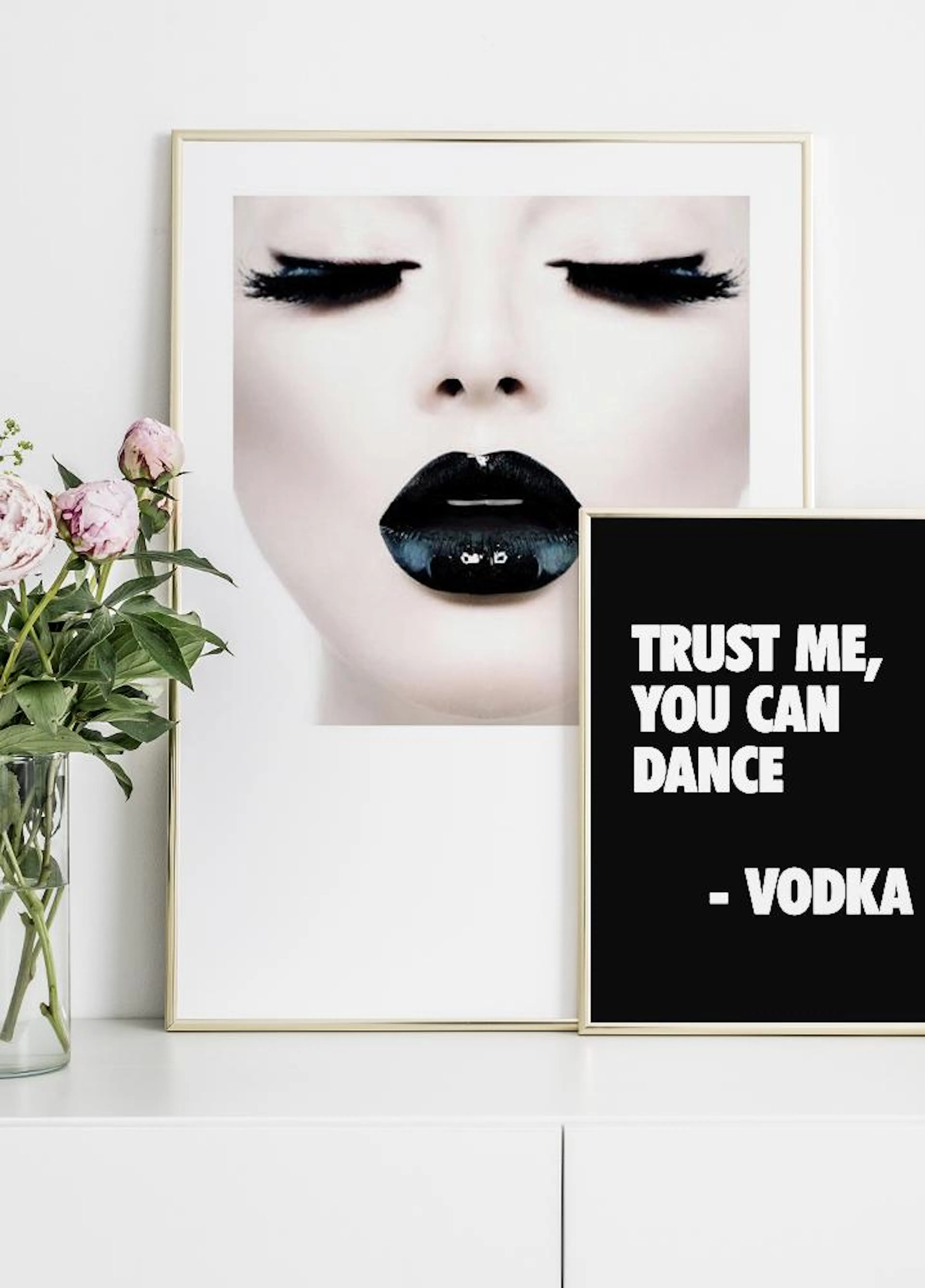 Two posters displayed on a white cabinet, one of a womans face with dramatic black makeup, and a black poster with white text TR