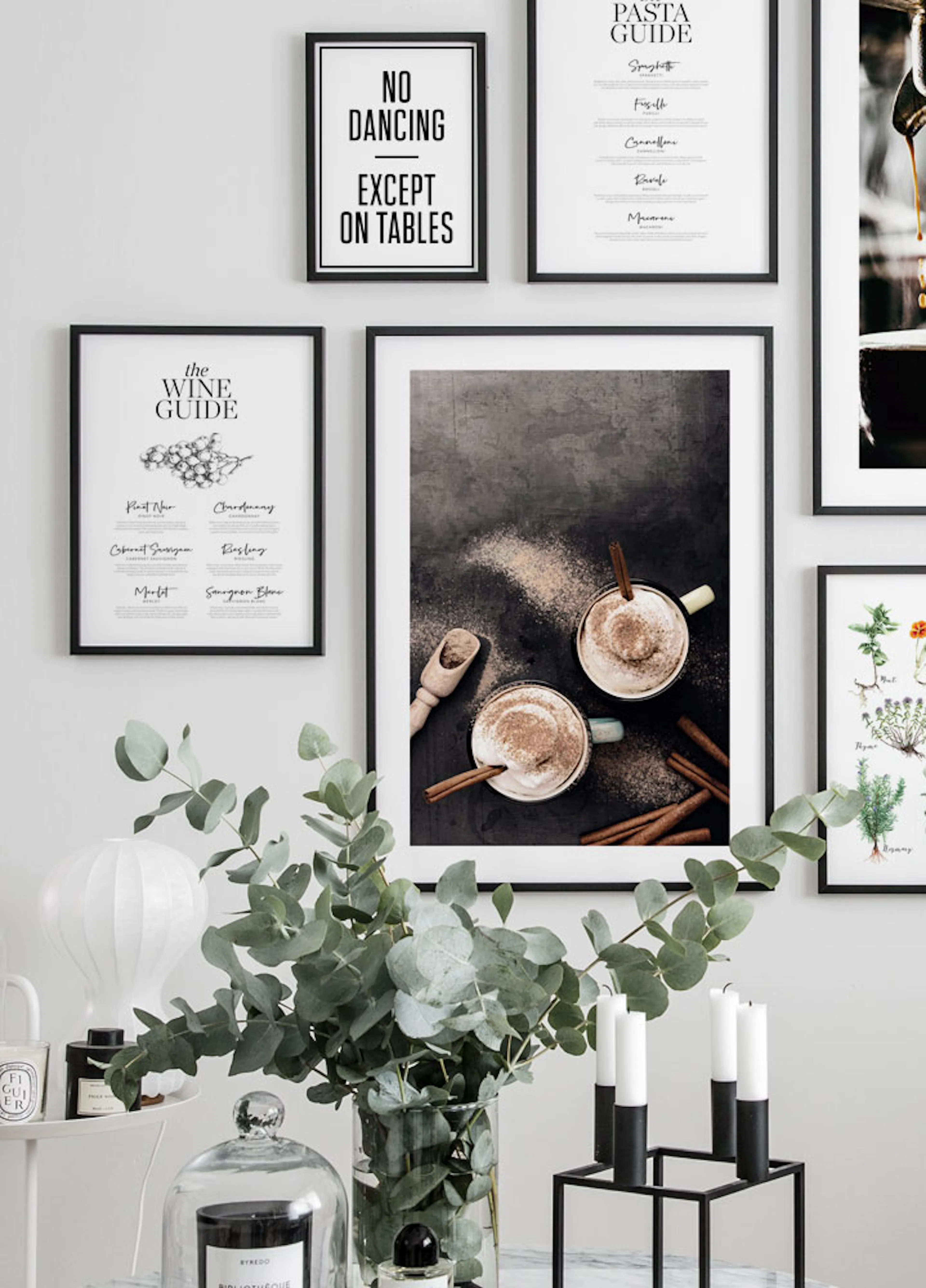 A poster of two hot drinks with cinnamon sticks and powder on a dark surface, displayed in a gallery wall setting.