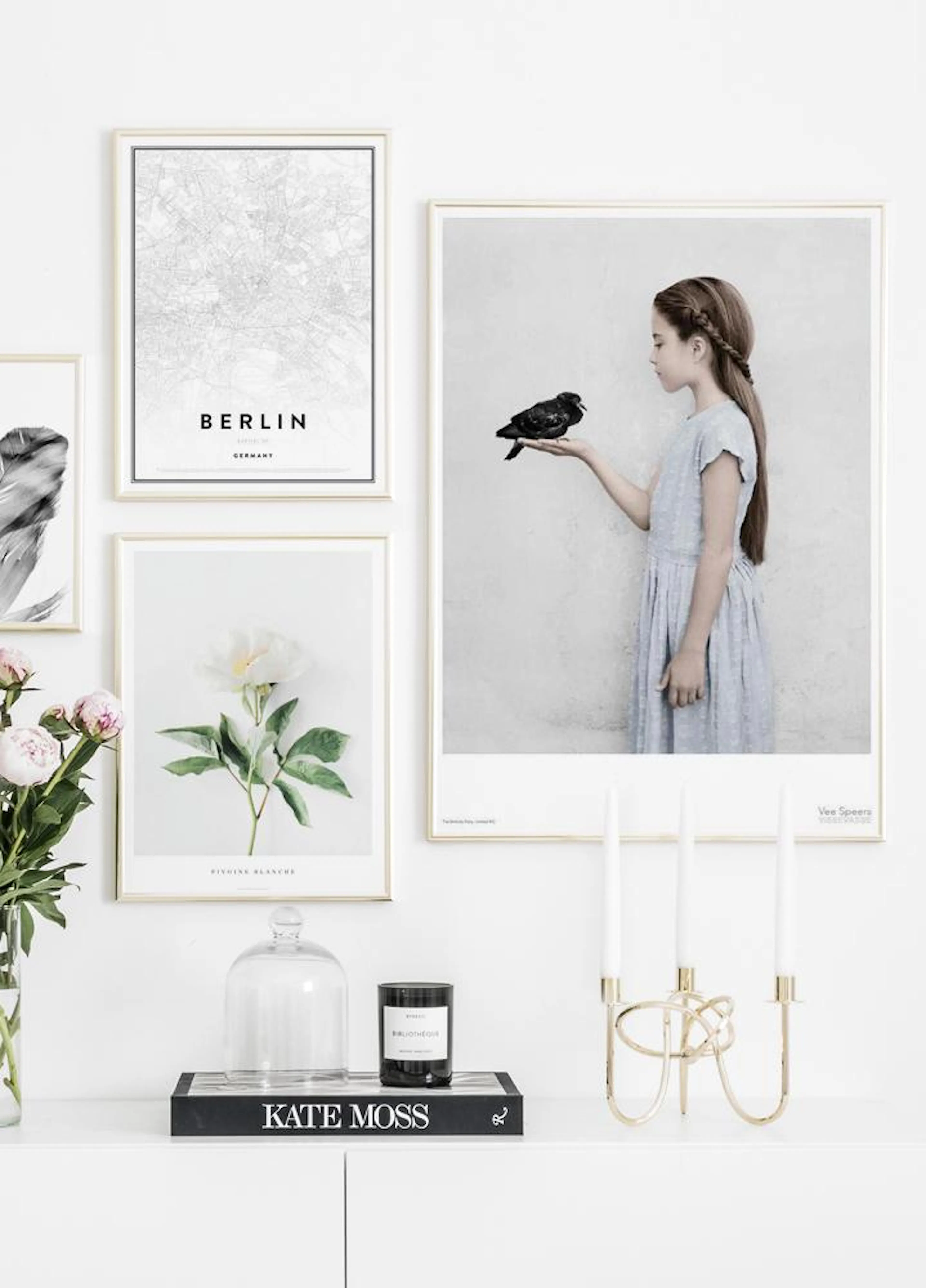 Julistetauluseinä, jossa mustavalkoinen Berliinin karttajuliste, valkoinen pionijuliste ja tyttö mustan linnun kanssa, valkoisel