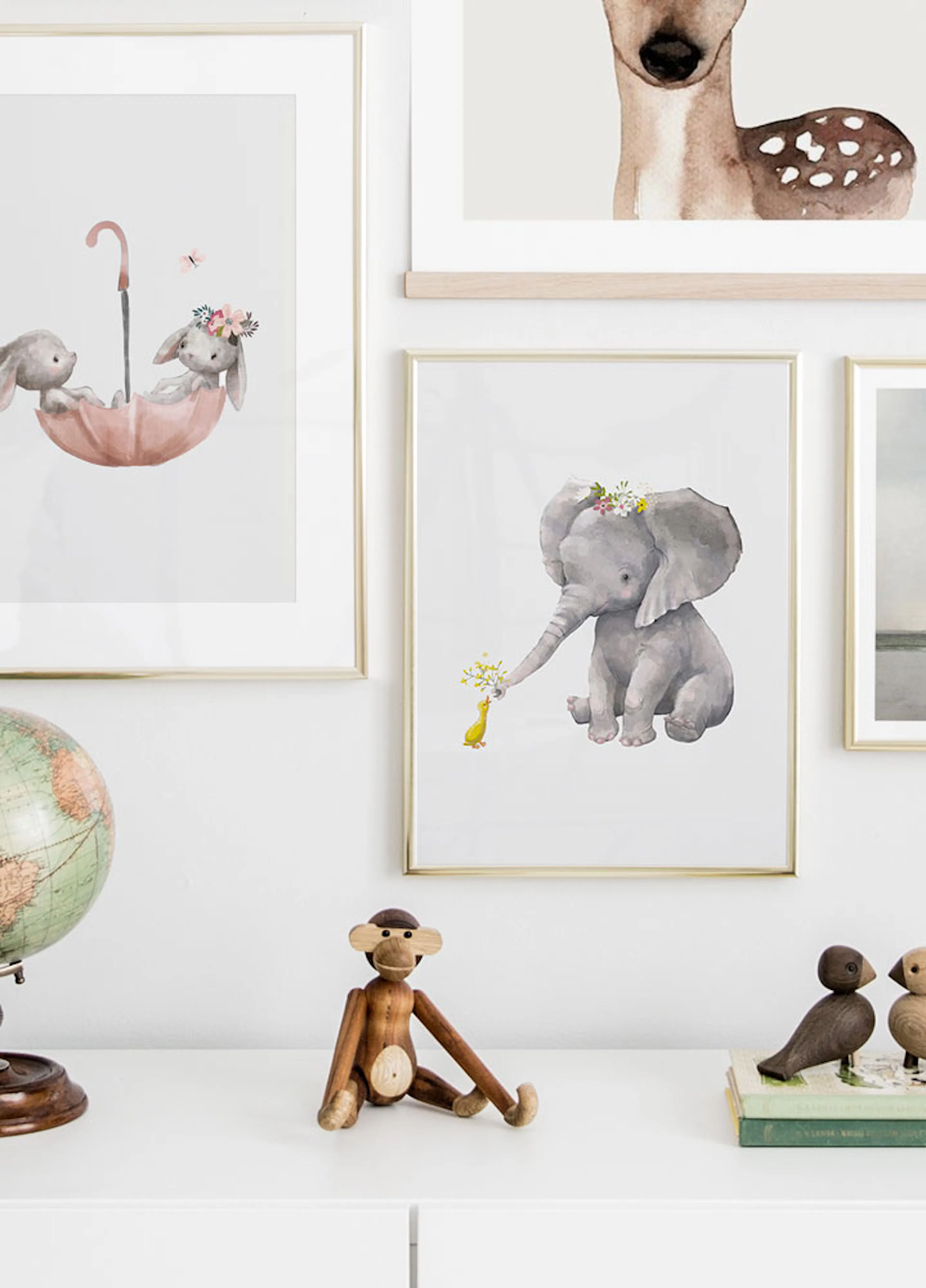 A gallery wall with three watercolour animal prints, including a deer, bunnies in an umbrella, and an elephant with a duck, disp