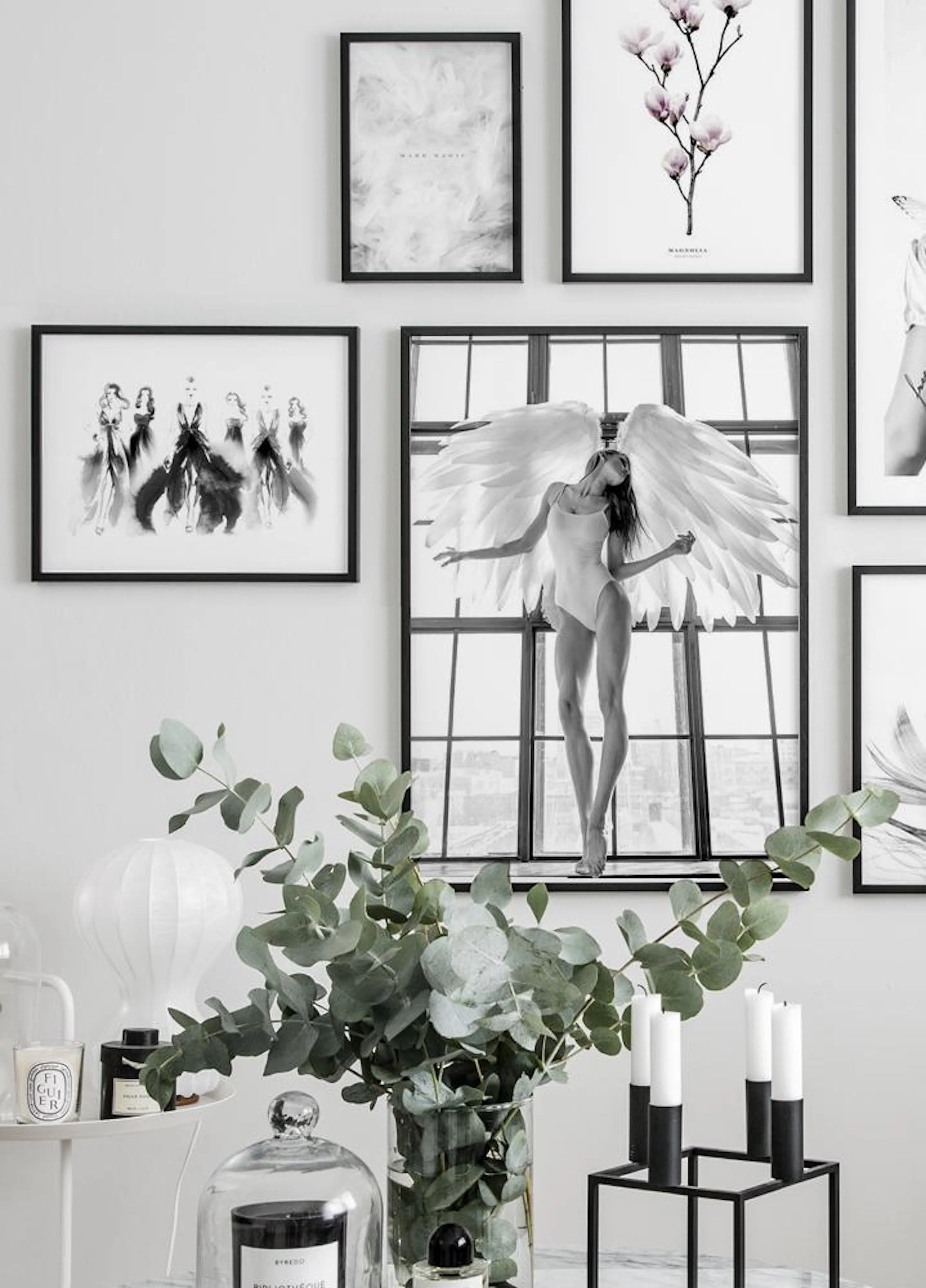 Mustavalkoinen juliste, jossa enkeli seisoo ikkunalaudalla suurten siipien kanssa, osana tauluseinää.