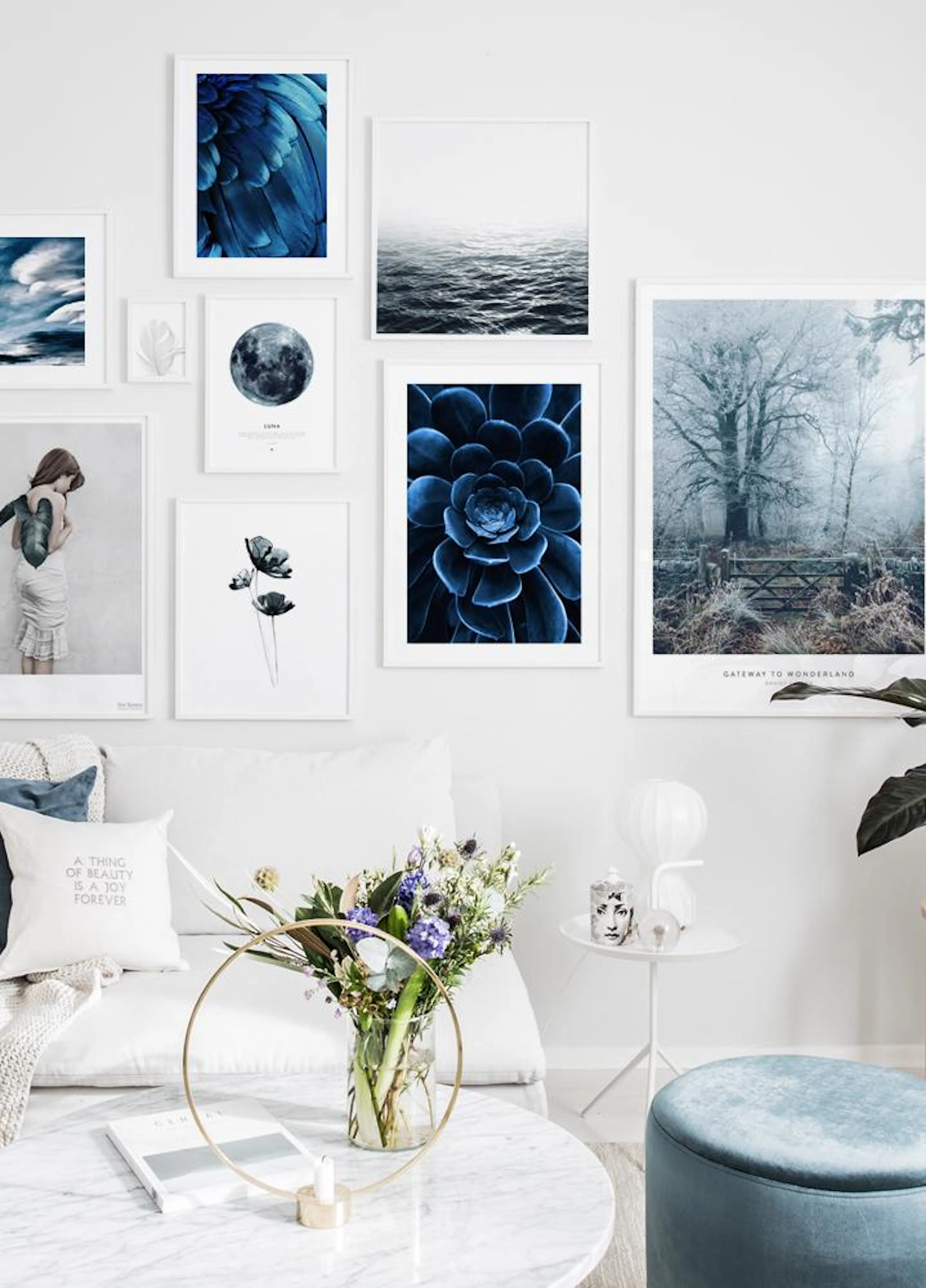 Nástěnná galerie modrých plakátů a fotografií v moderním obývacím pokoji s bílou pohovkou, polštáři a květinami na mramorovém st