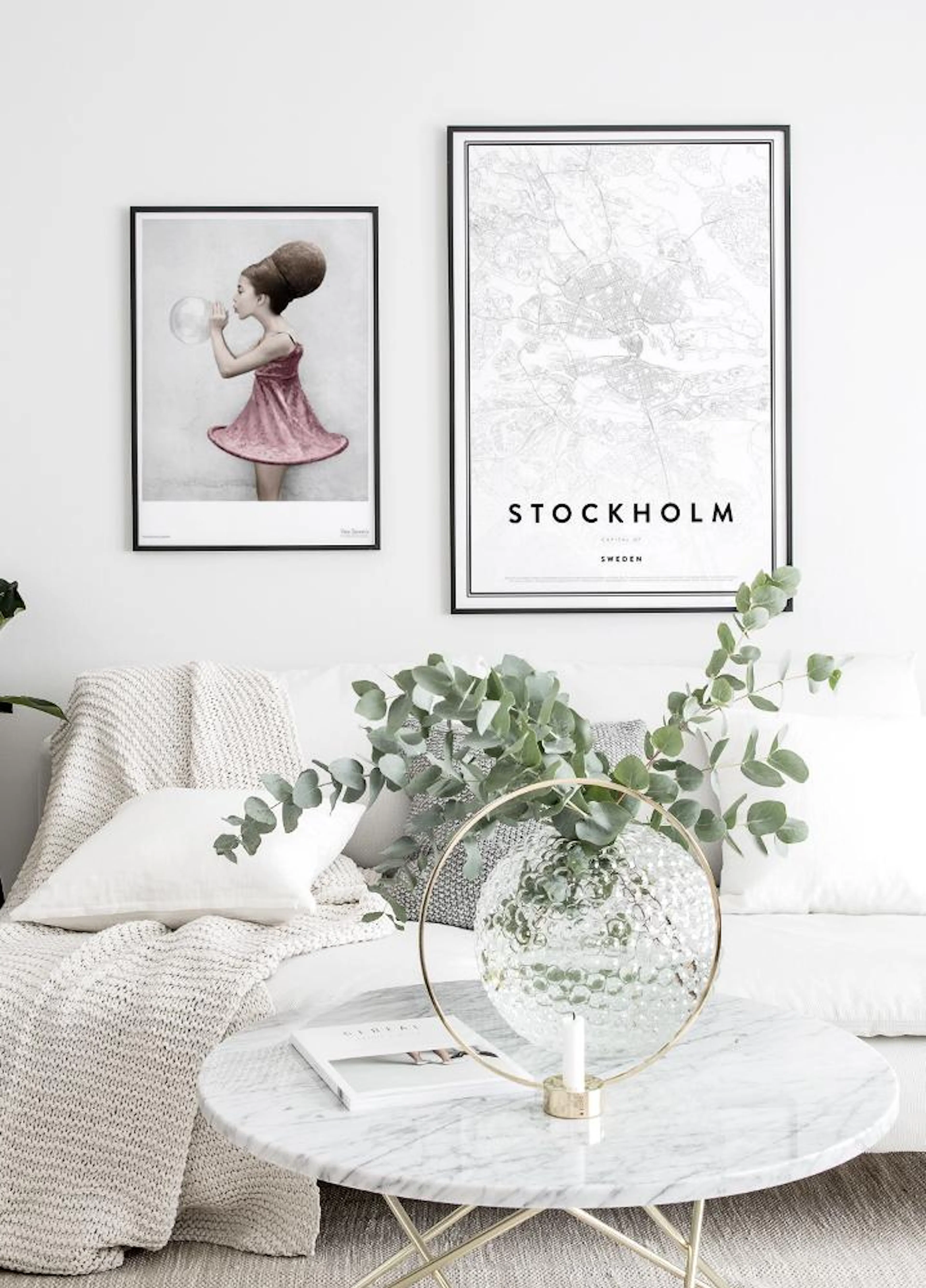 A poster of a girl blowing a bubble and a Stockholm map poster, displayed above a white sofa in a living room.