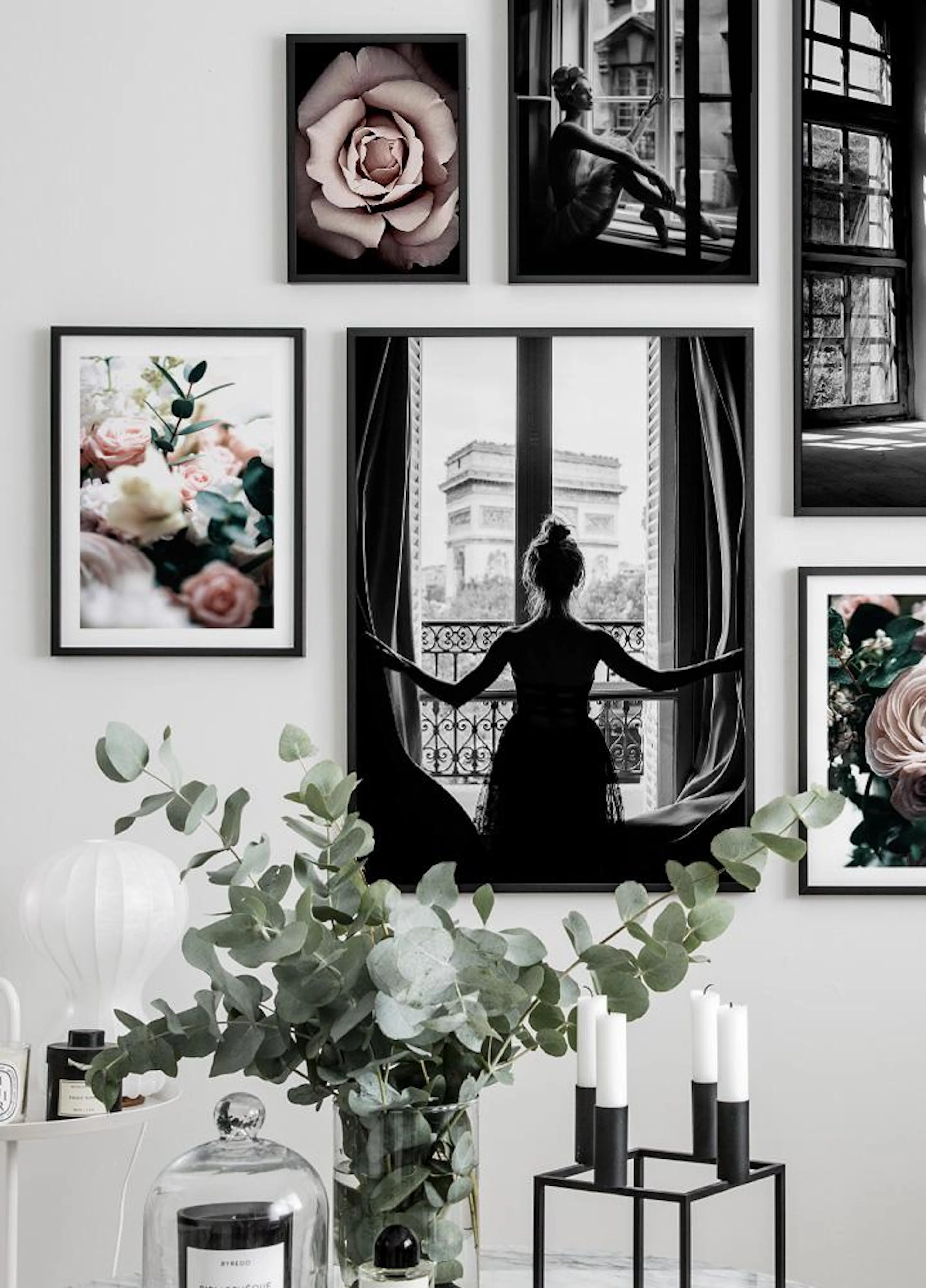 A gallery wall of black and white cityscape and floral posters, with a plant and candles in the foreground.