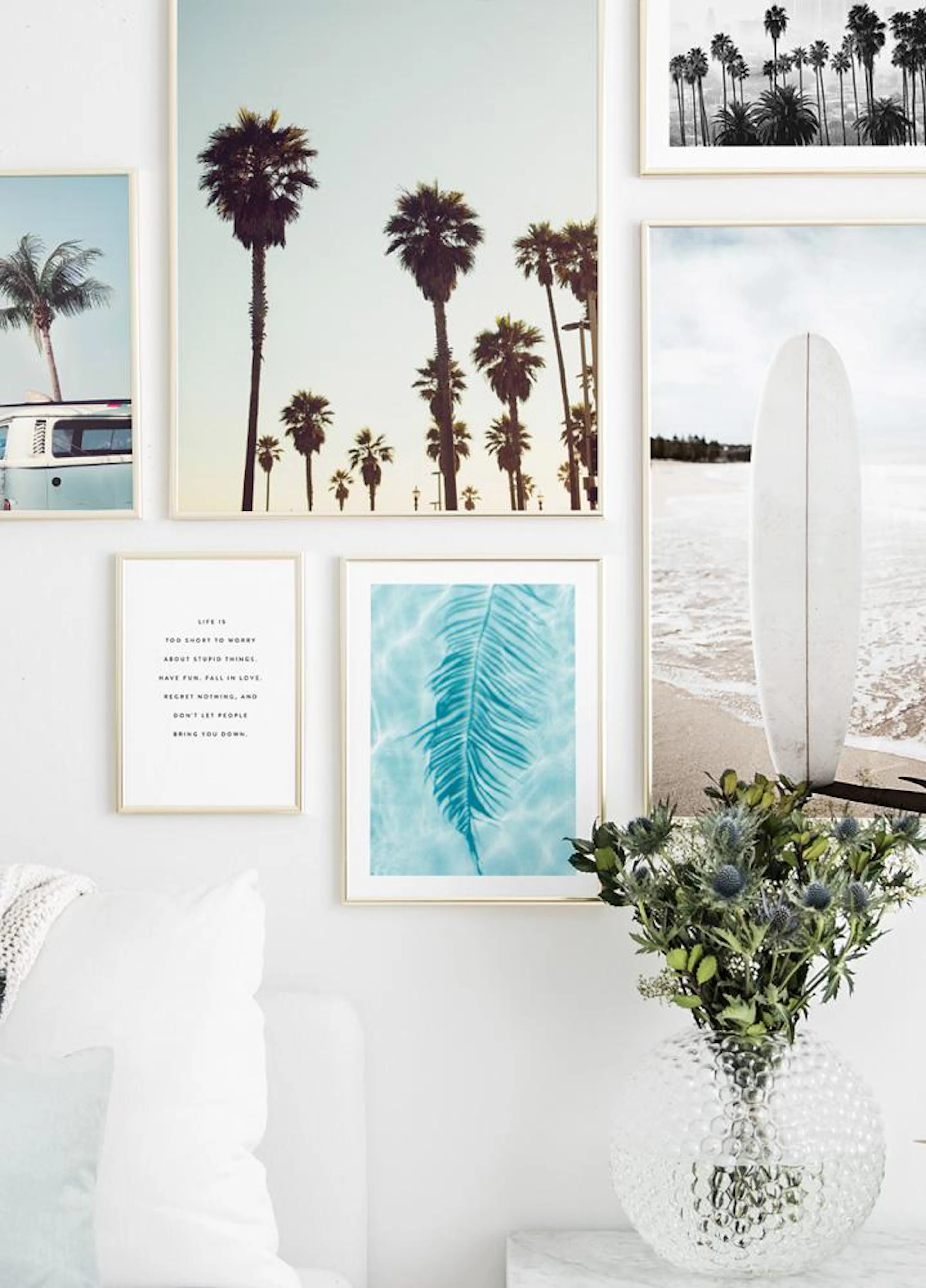 A gallery wall featuring five coastal and nature-themed posters, including palm trees, a surfboard, and a fern, displayed above 