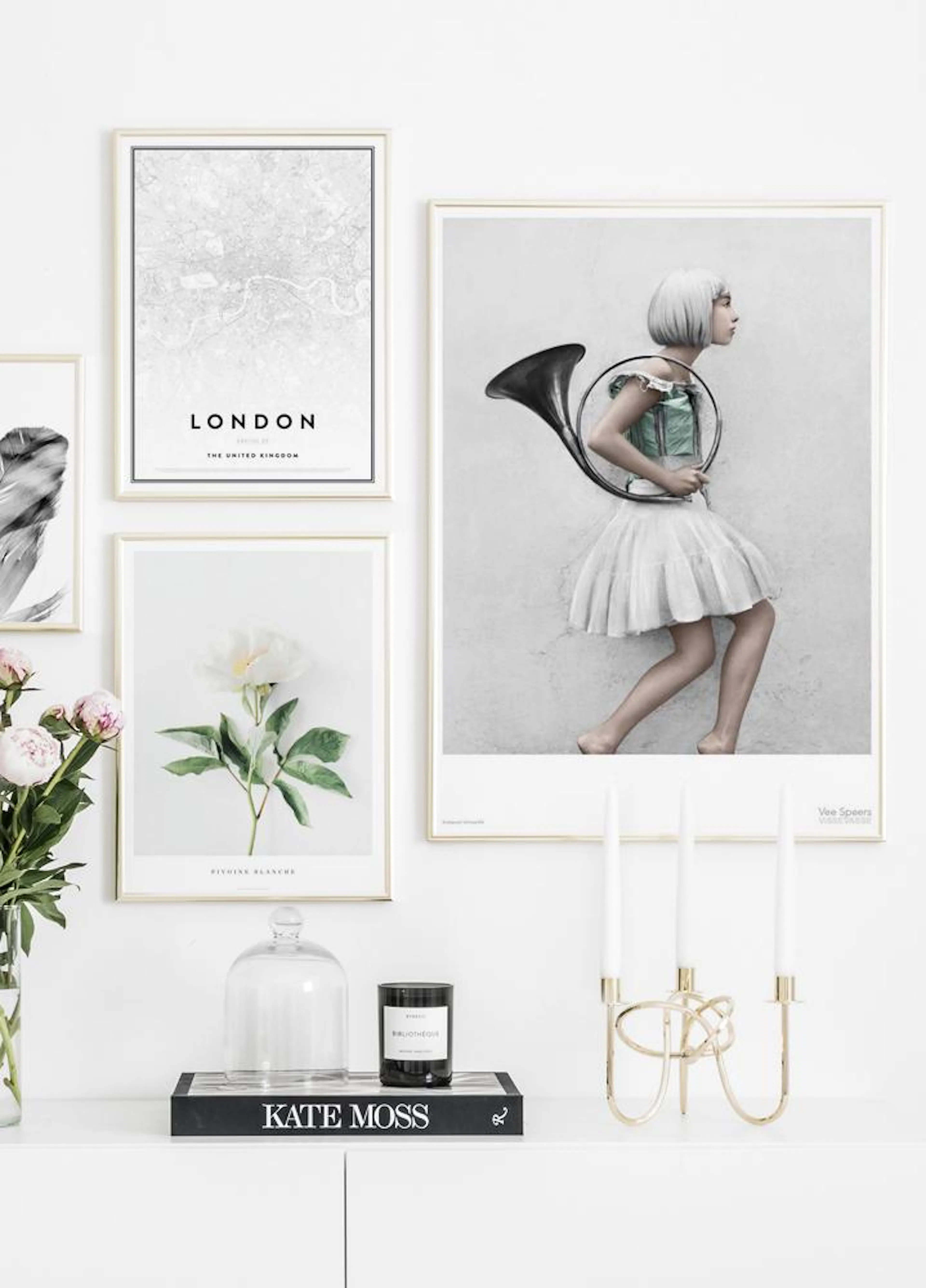 A gallery wall of posters: a London map, a woman with a French horn, a single white flower, and a feather, above a white cabinet
