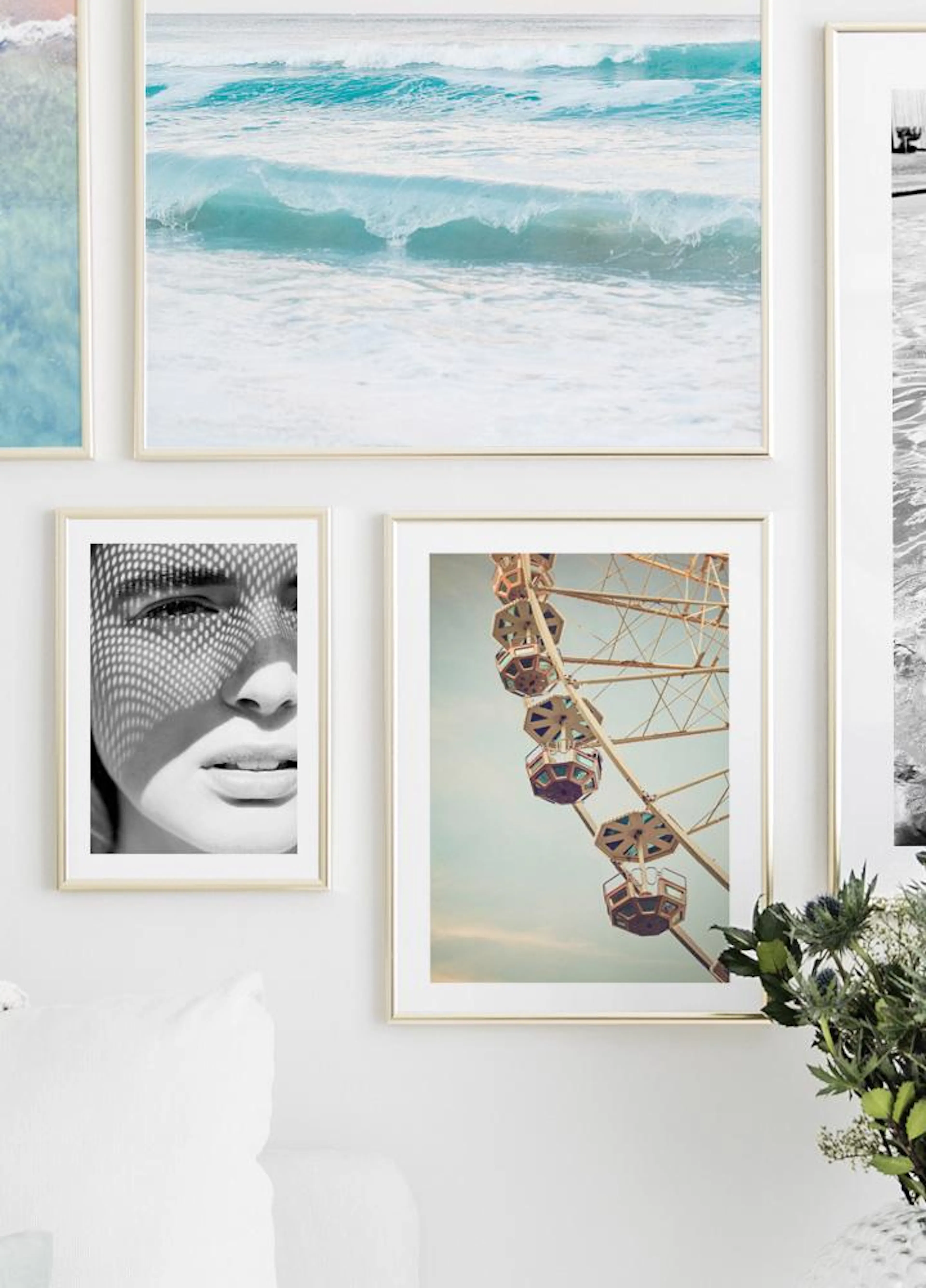 A gallery wall with prints of ocean waves, a black and white portrait, and a Ferris wheel, hanging above a white sofa.