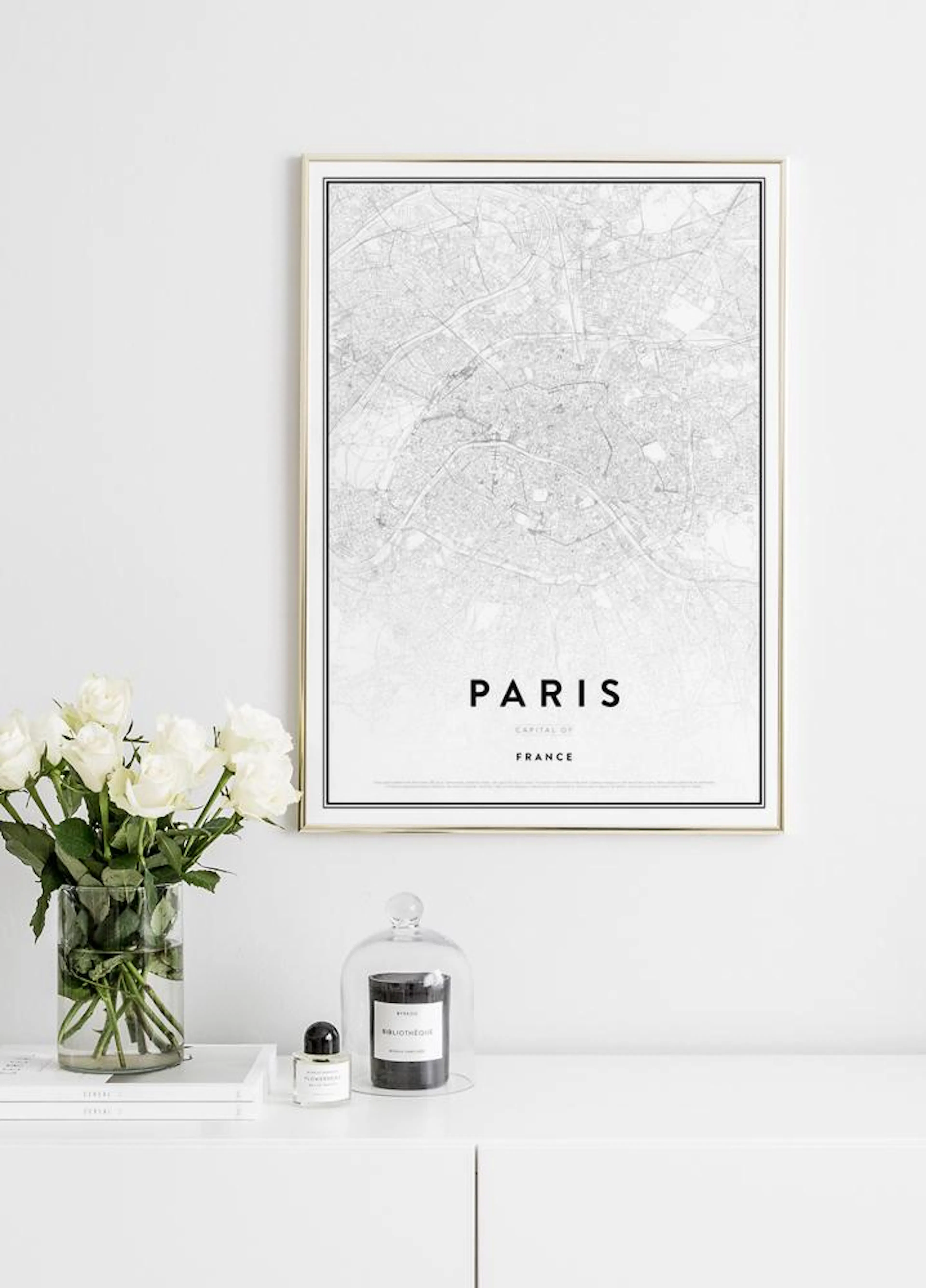 Poster cu harta Parisului în alb-negru, atârnat pe un perete alb, deasupra unei comode cu flori și lumânări.