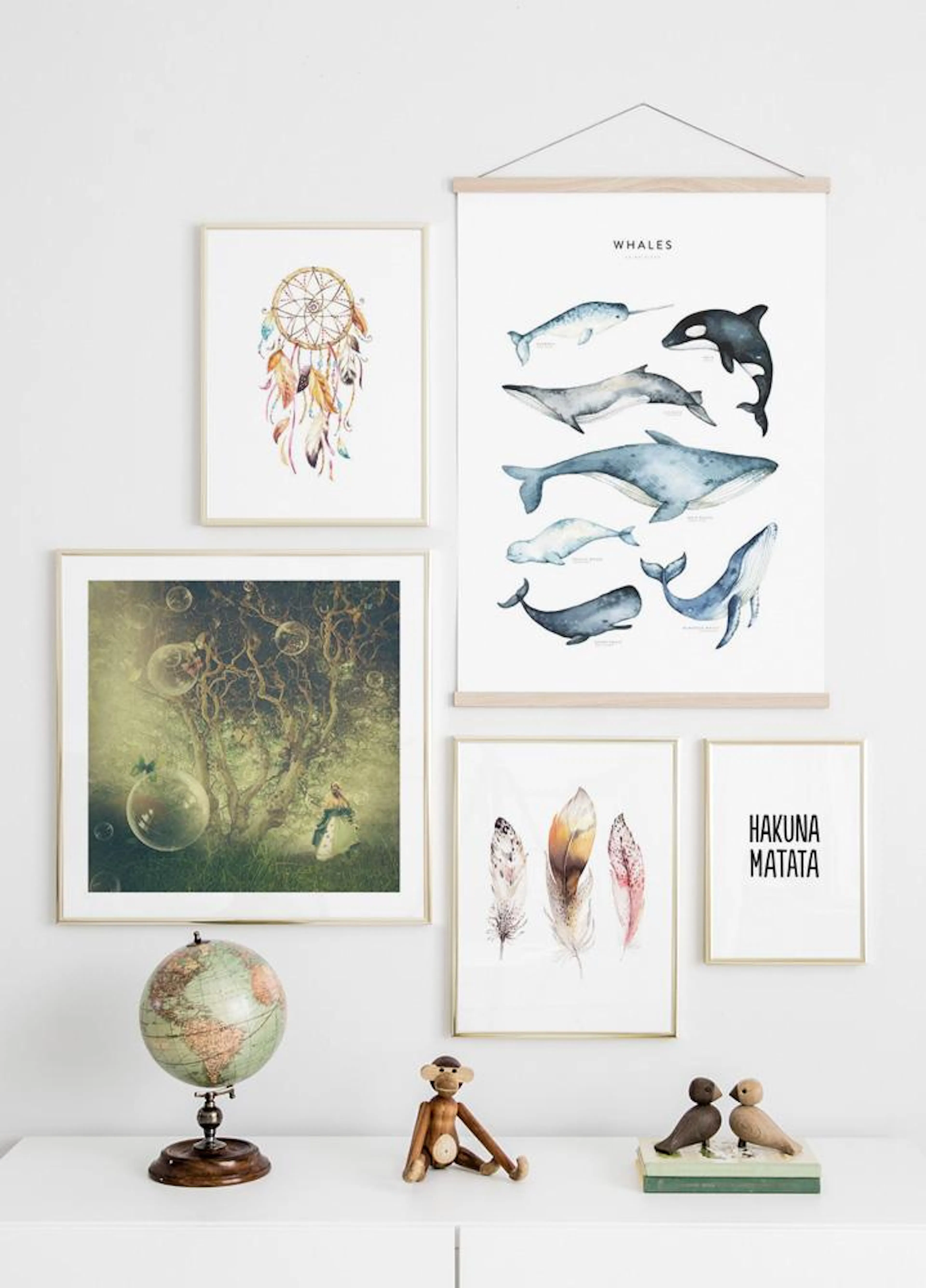 A gallery wall with a whale chart poster, a dreamcatcher print, a magical forest scene, feather art, and Hakuna Matata typograph
