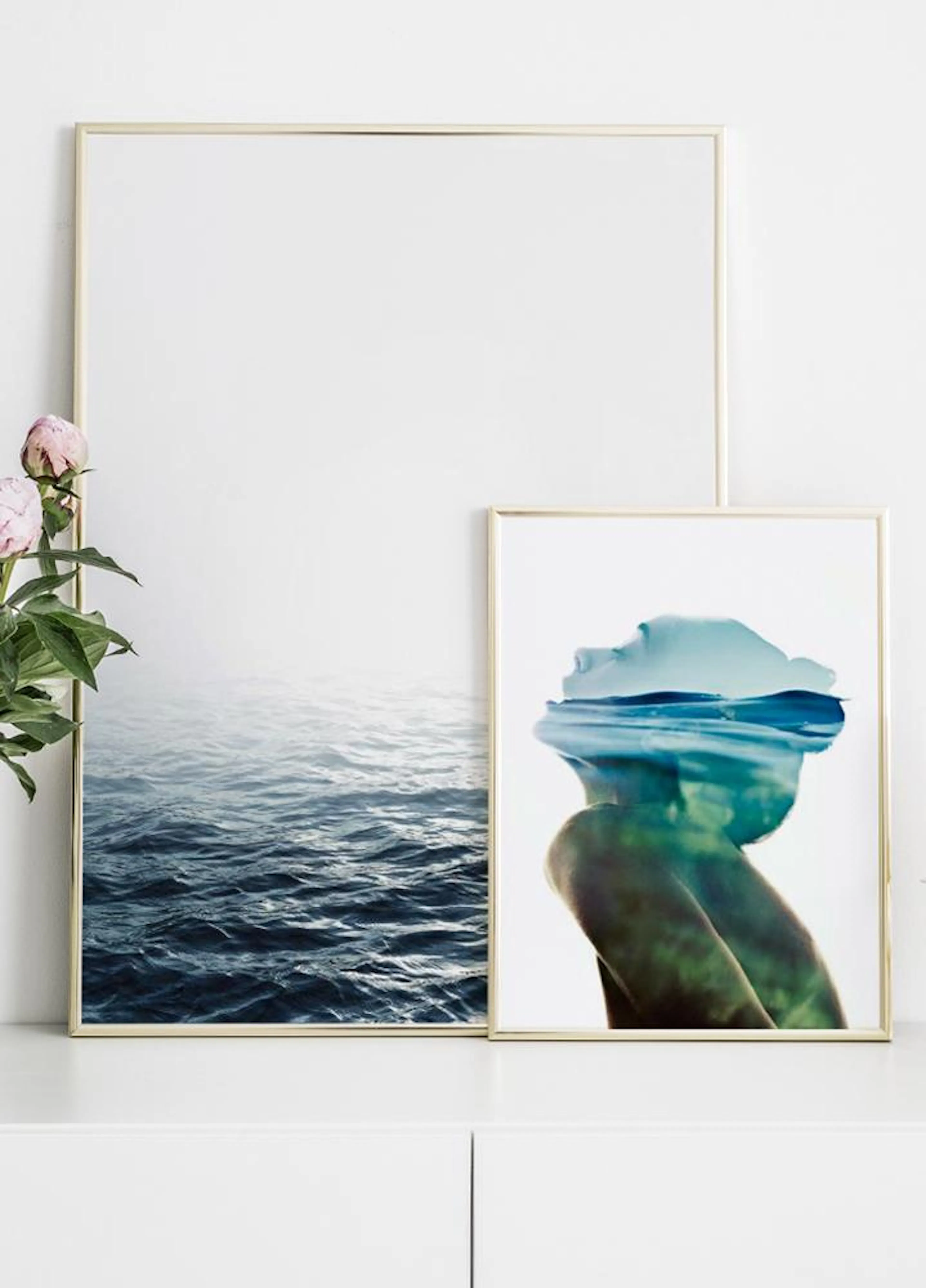 Two posters leaning against a white wall. The left poster shows deep blue ocean waves, and the right poster features a profile o