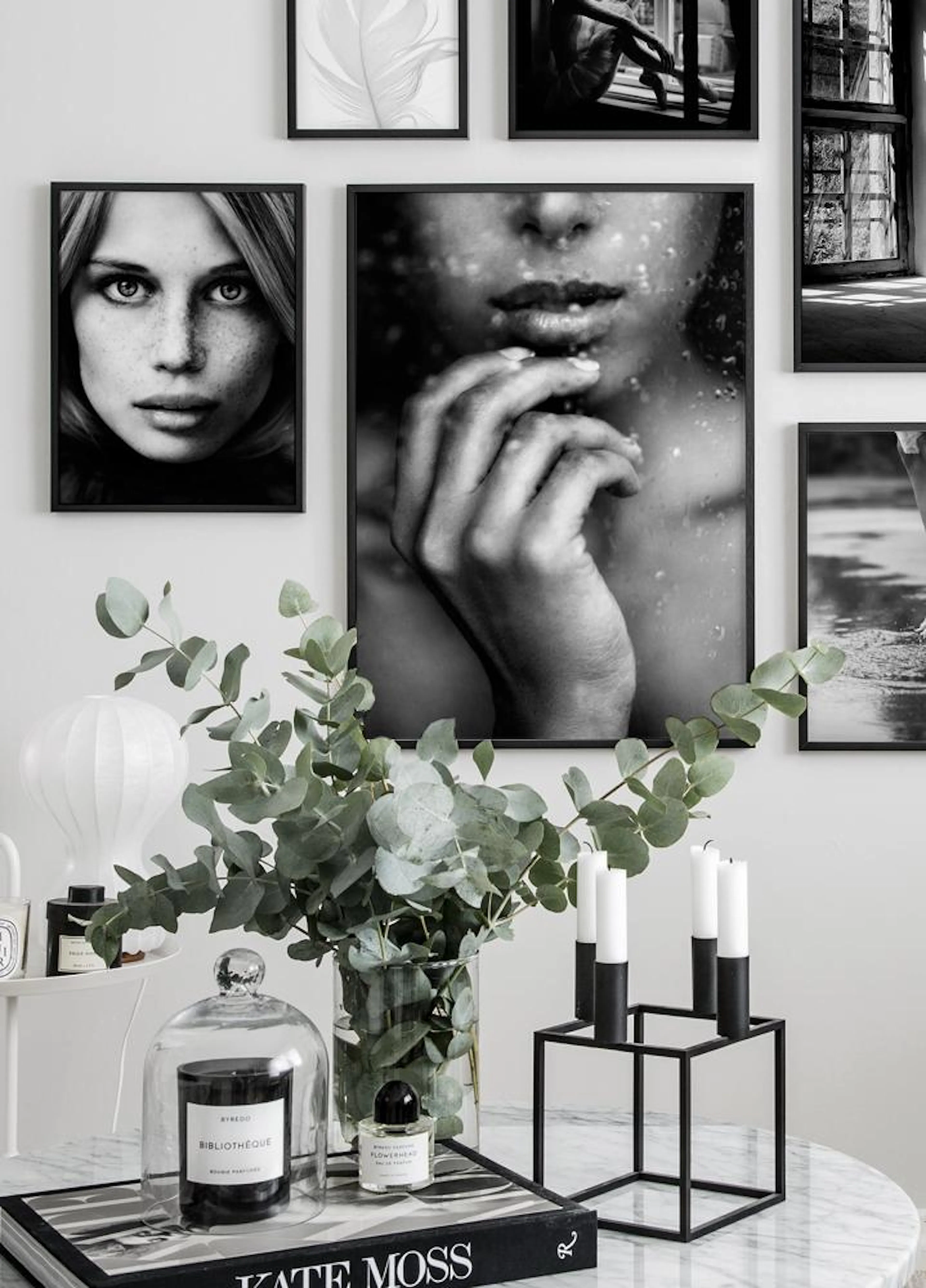A gallery wall of black and white posters, including a woman with freckles and a close-up of a face behind wet glass, above a ma