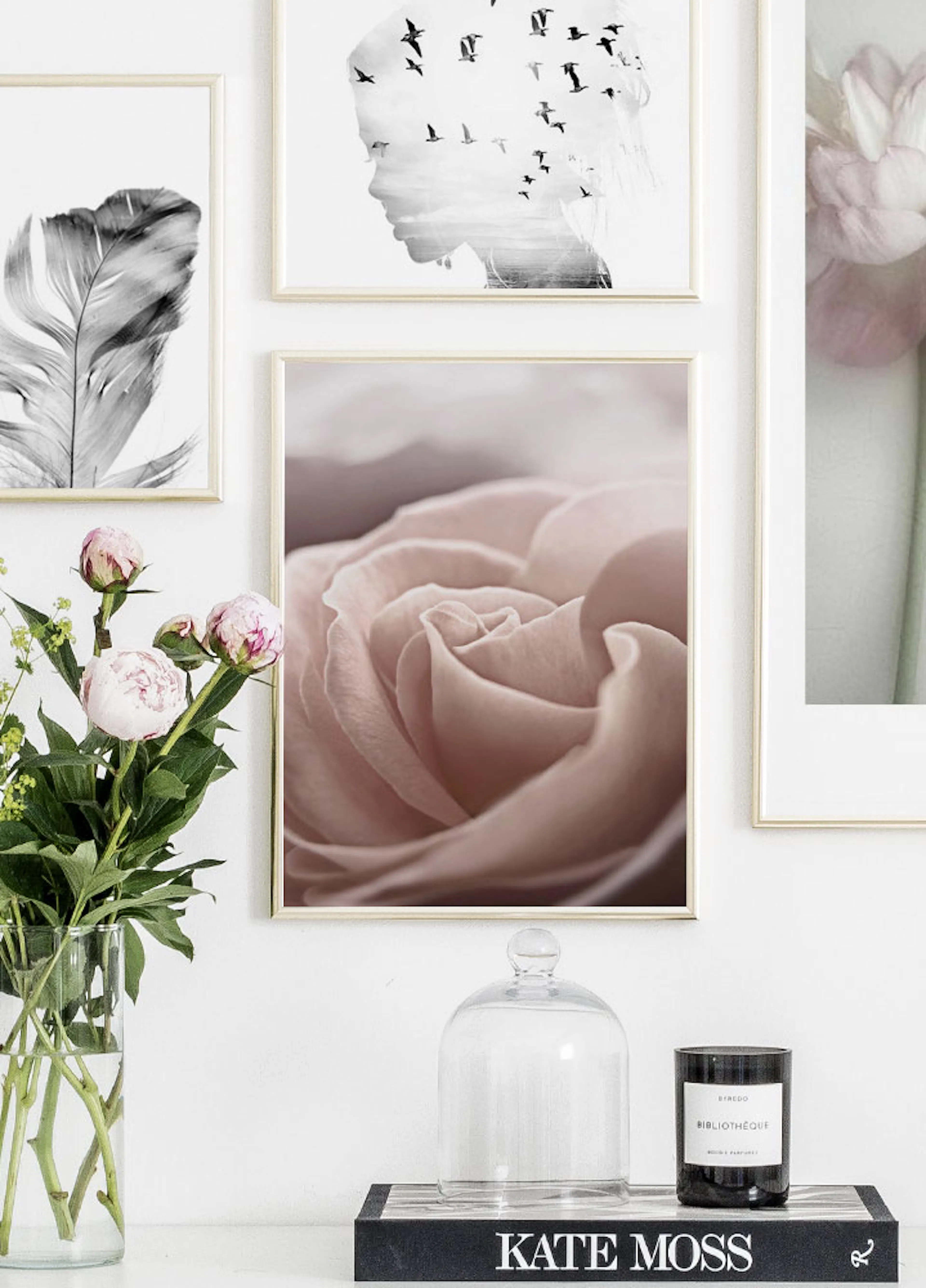 A gallery wall featuring a soft pink rose poster, a black and white feather, and a silhouette of a face with birds, above a glas