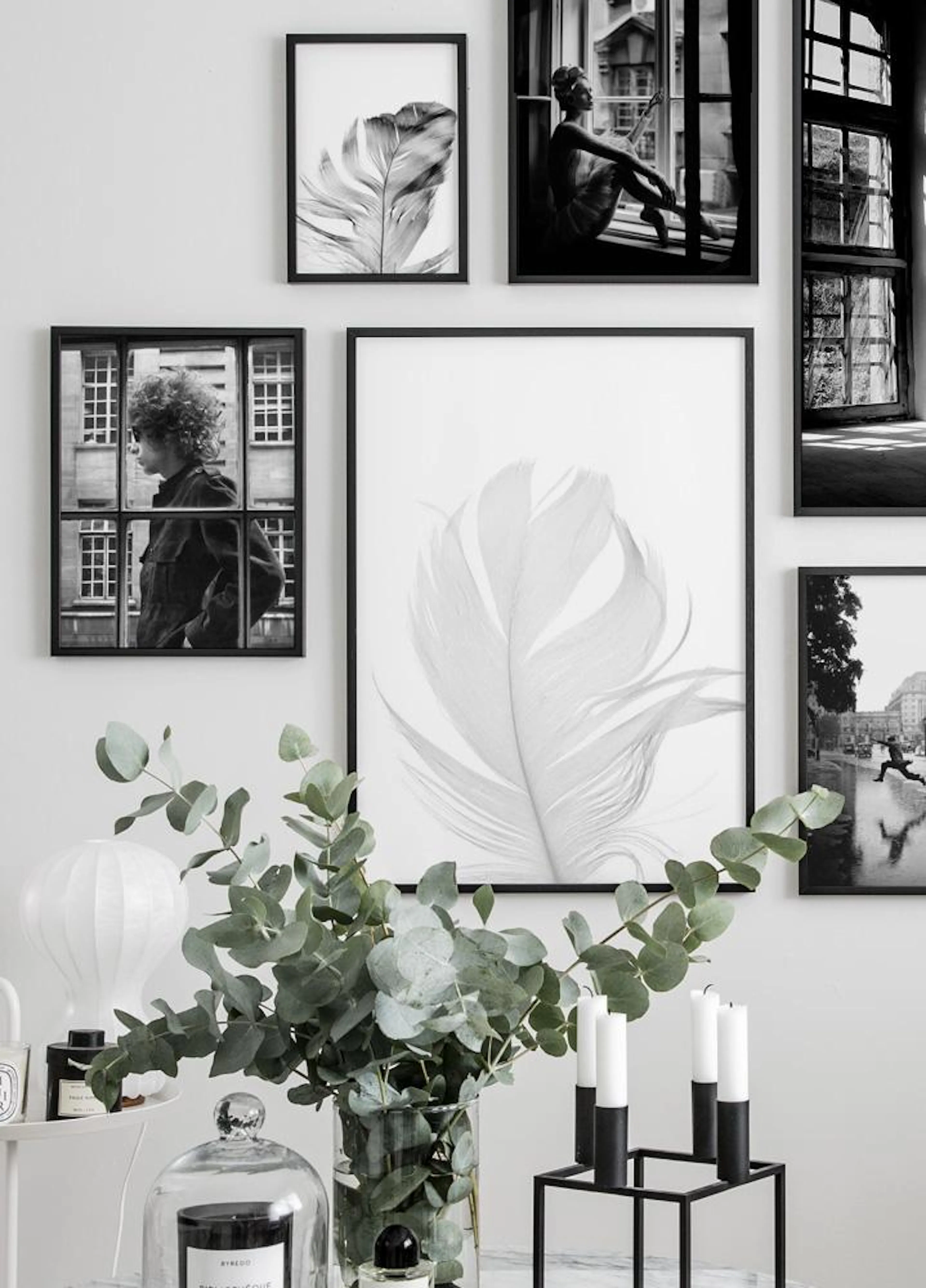 A gallery wall featuring black and white posters, including a large feather, in a modern living room with eucalyptus in a vase.