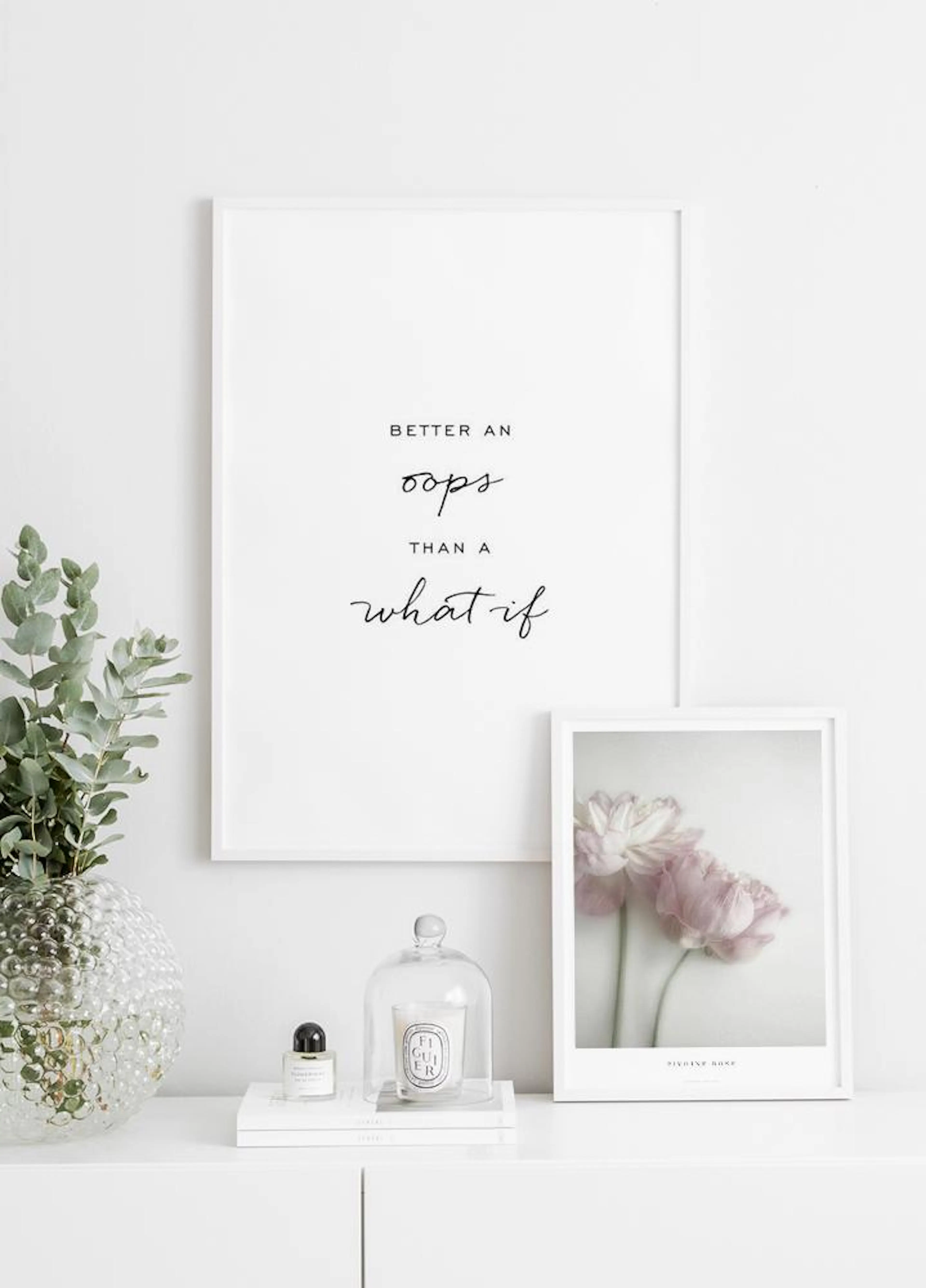 A poster with the quote Better an oops than a what if in black script, hanging above a white console table with decor.