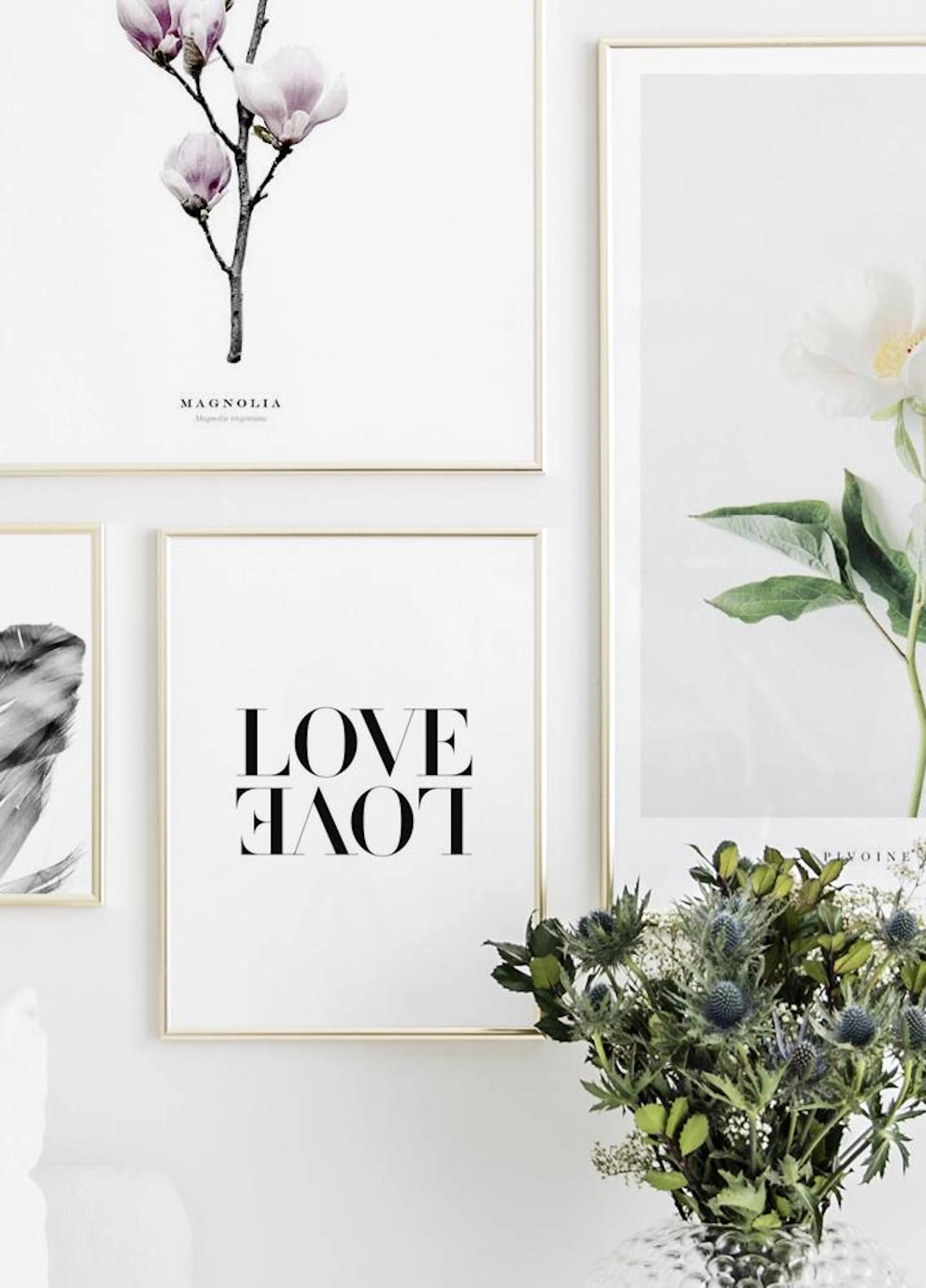 A gallery wall with three posters: a magnolia branch, black LOVE text, and a white peony, next to a vase of thistles.