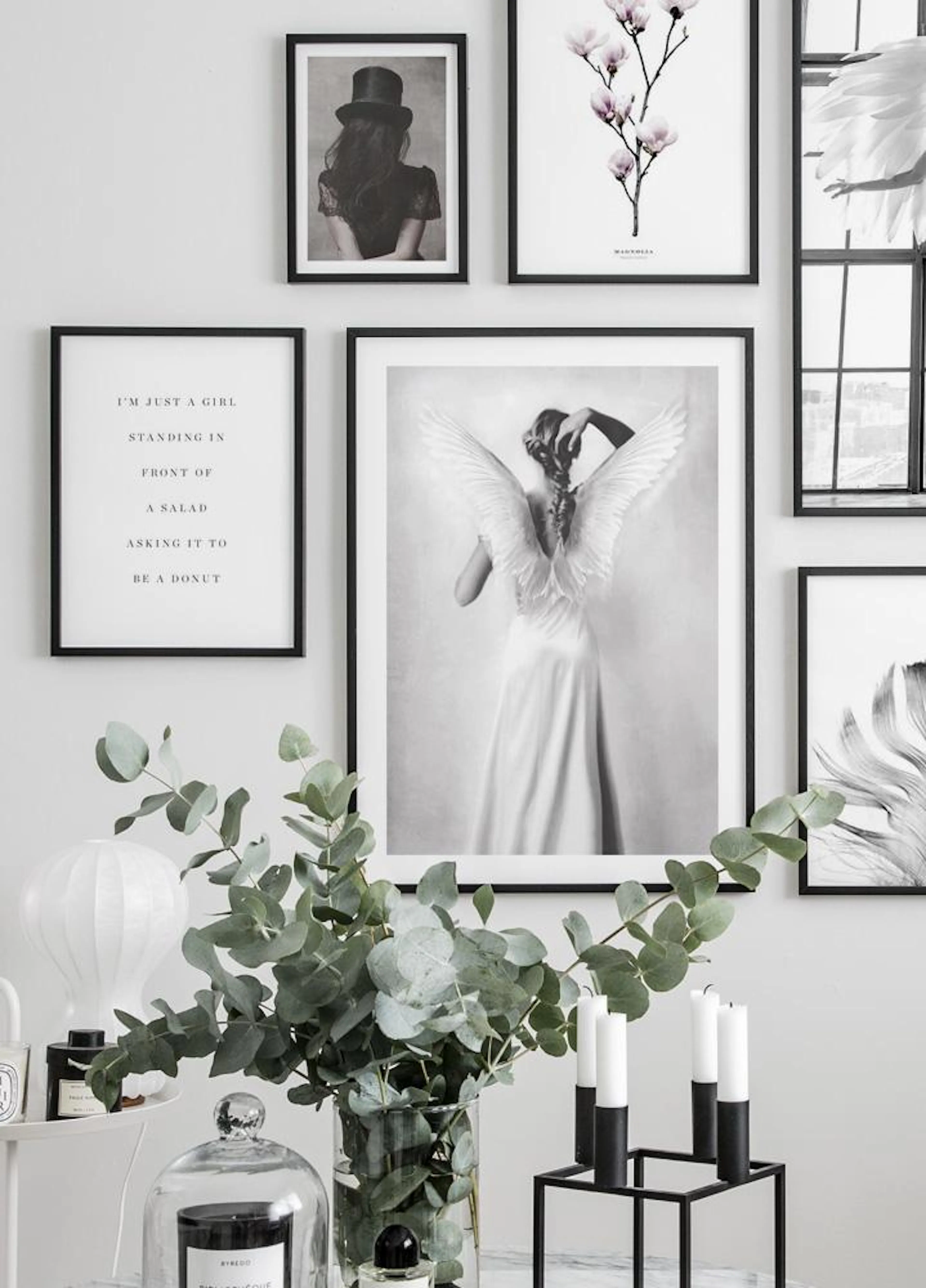A gallery wall featuring a woman with angel wings, a girl in a top hat, a magnolia branch, and a text poster, displayed in a liv