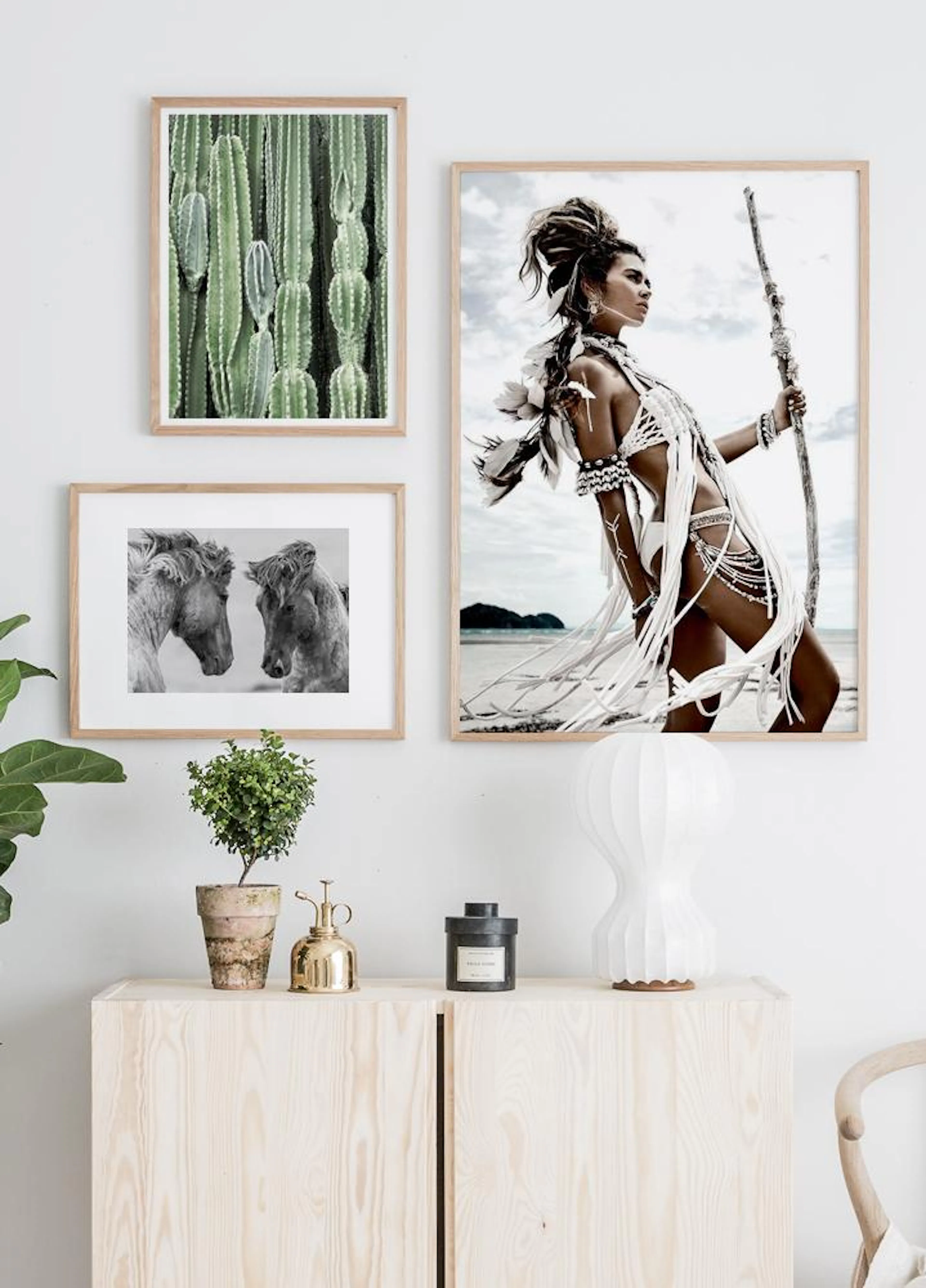 A gallery wall with three posters: a green cactus print, two horses, and a woman in tribal attire, above a wooden cabinet.