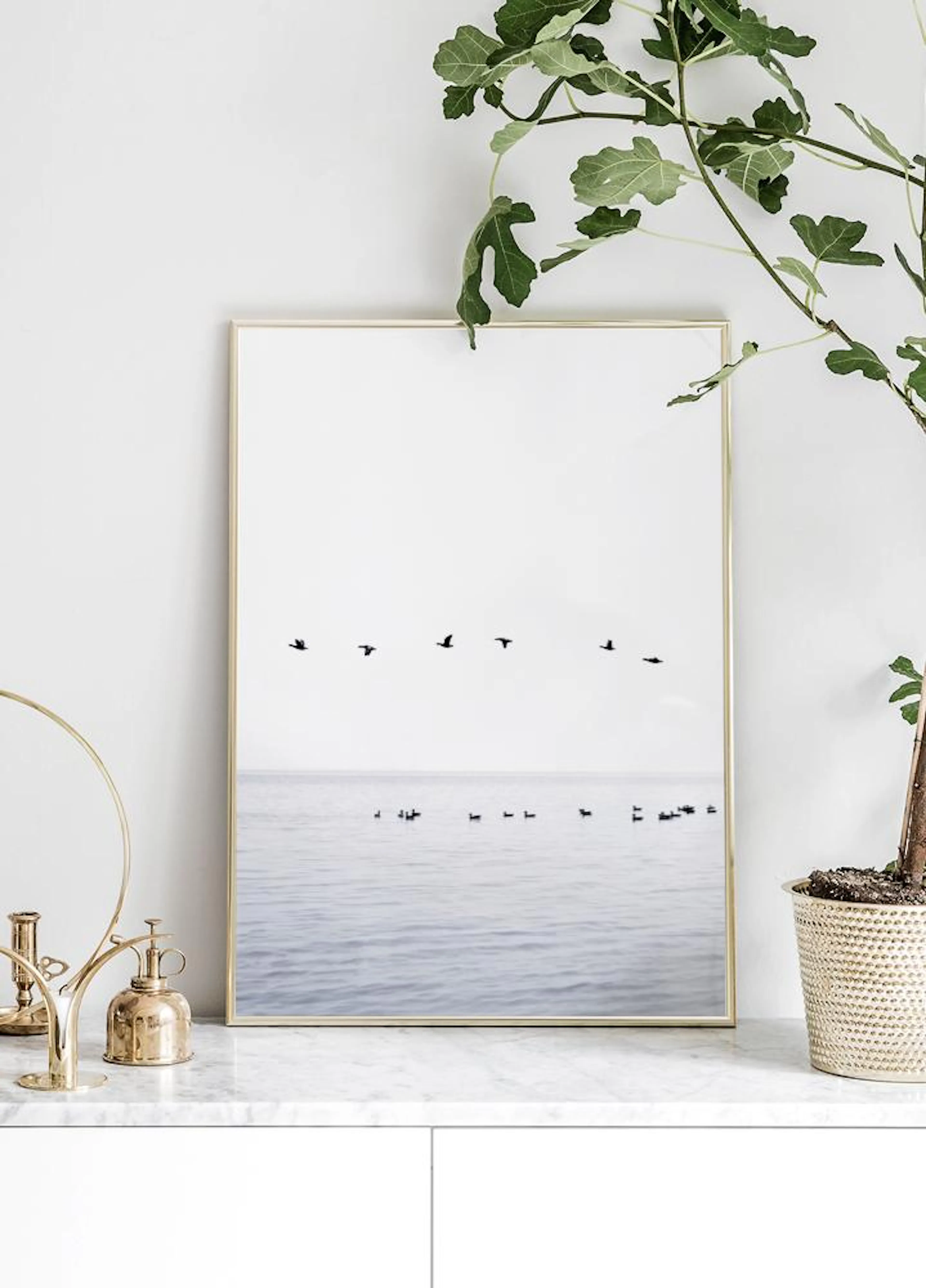 Póster de aves marinas volando sobre el agua y flotando en la superficie, exhibido sobre una superficie de mármol con una planta