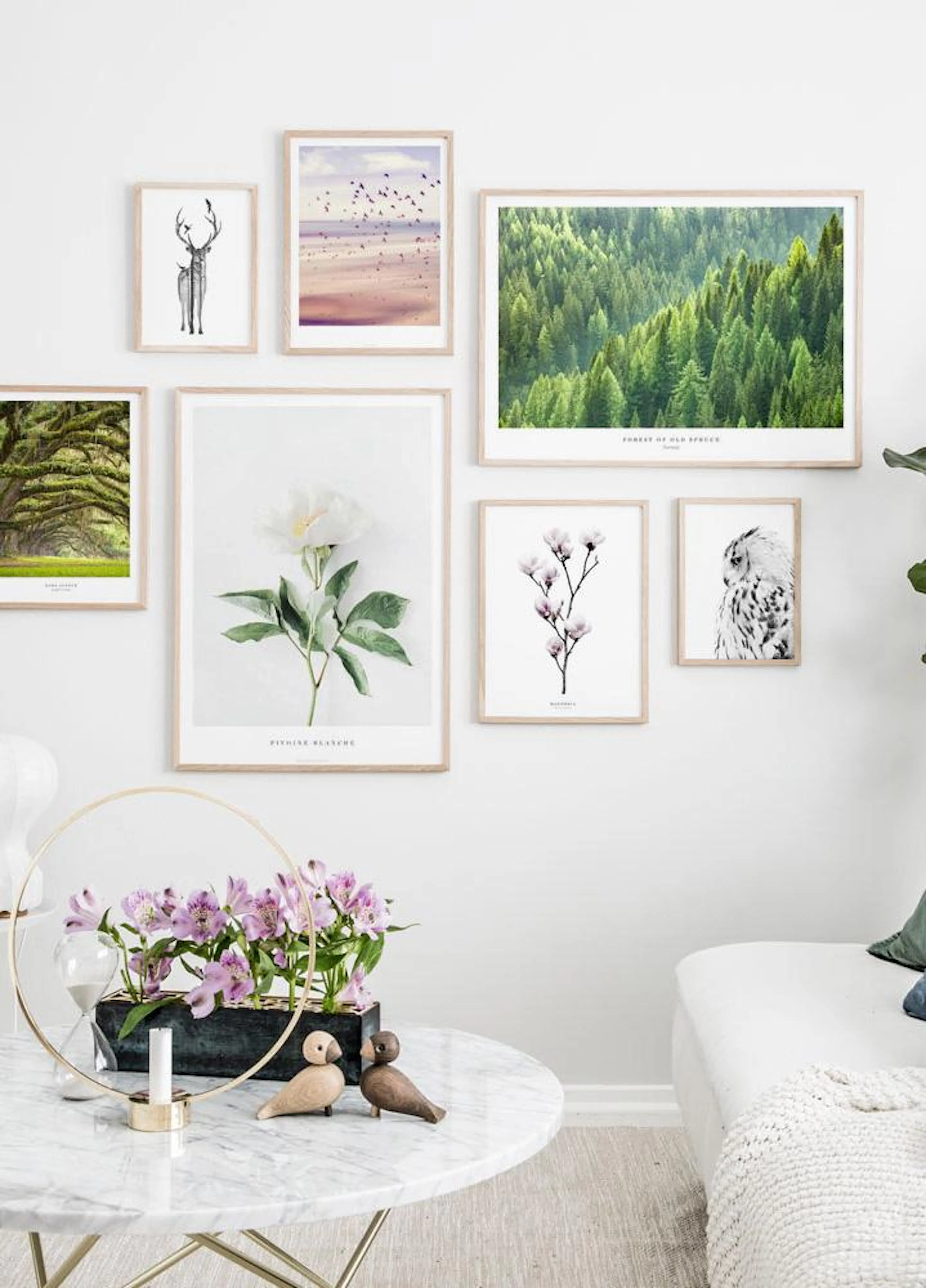 A gallery wall with seven nature-themed posters, including a forest, beach, deer, flowers, and an owl, displayed above a white s