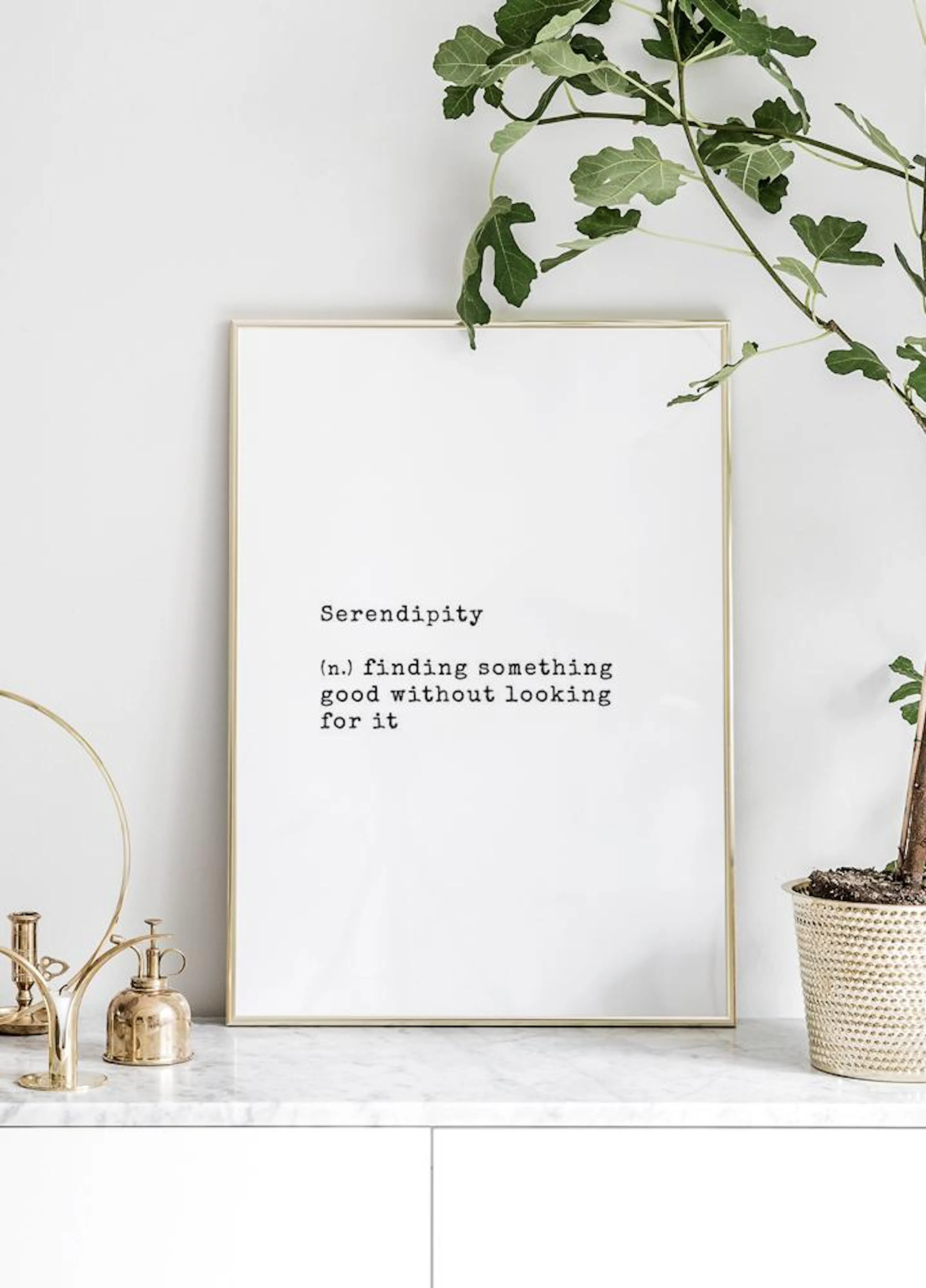 A white poster with black text defining Serendipity, displayed on a white marble surface next to a potted plant and gold decor.