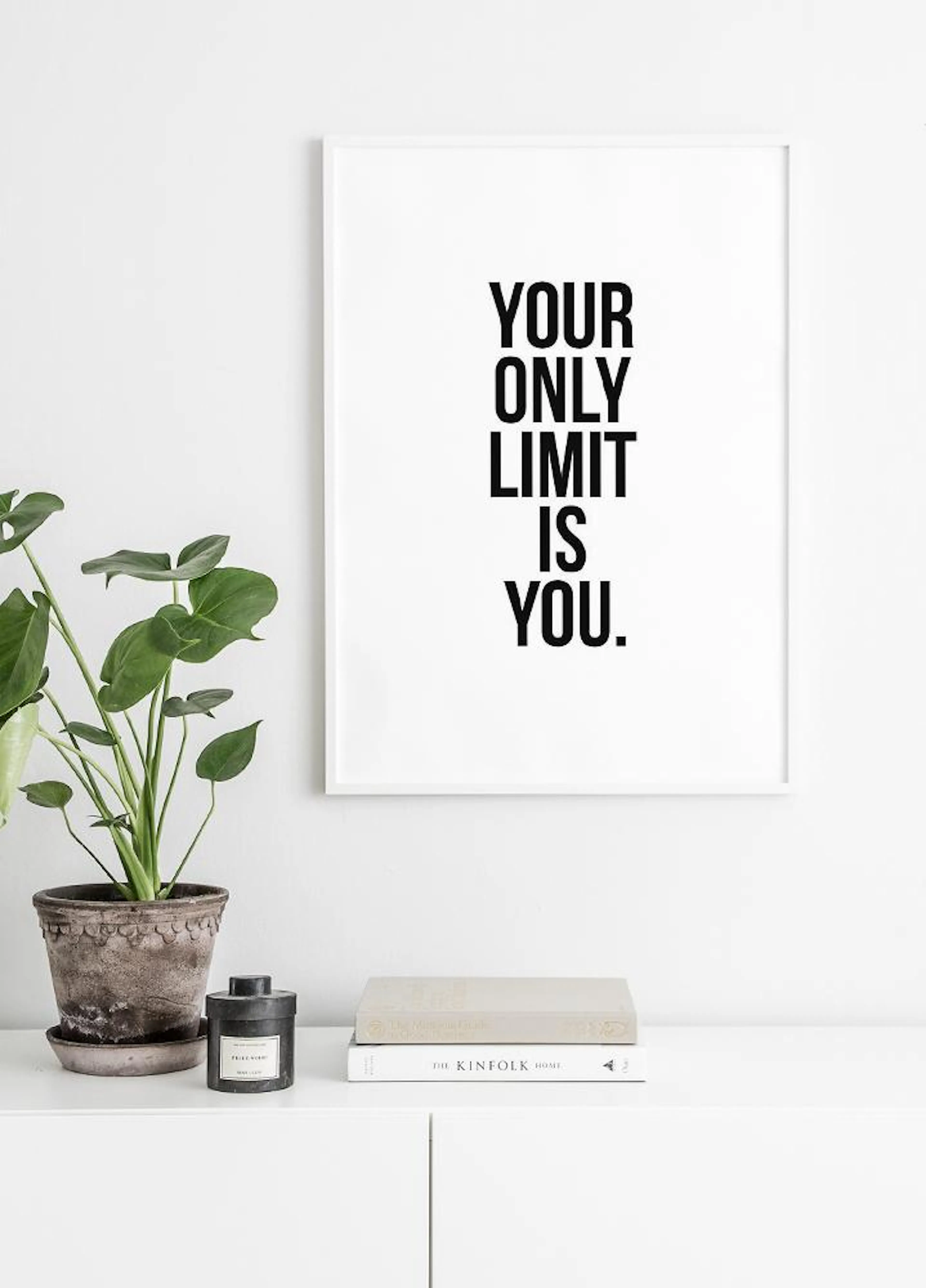A motivational poster with the text YOUR ONLY LIMIT IS YOU, hanging above a white cabinet with a potted plant and books.