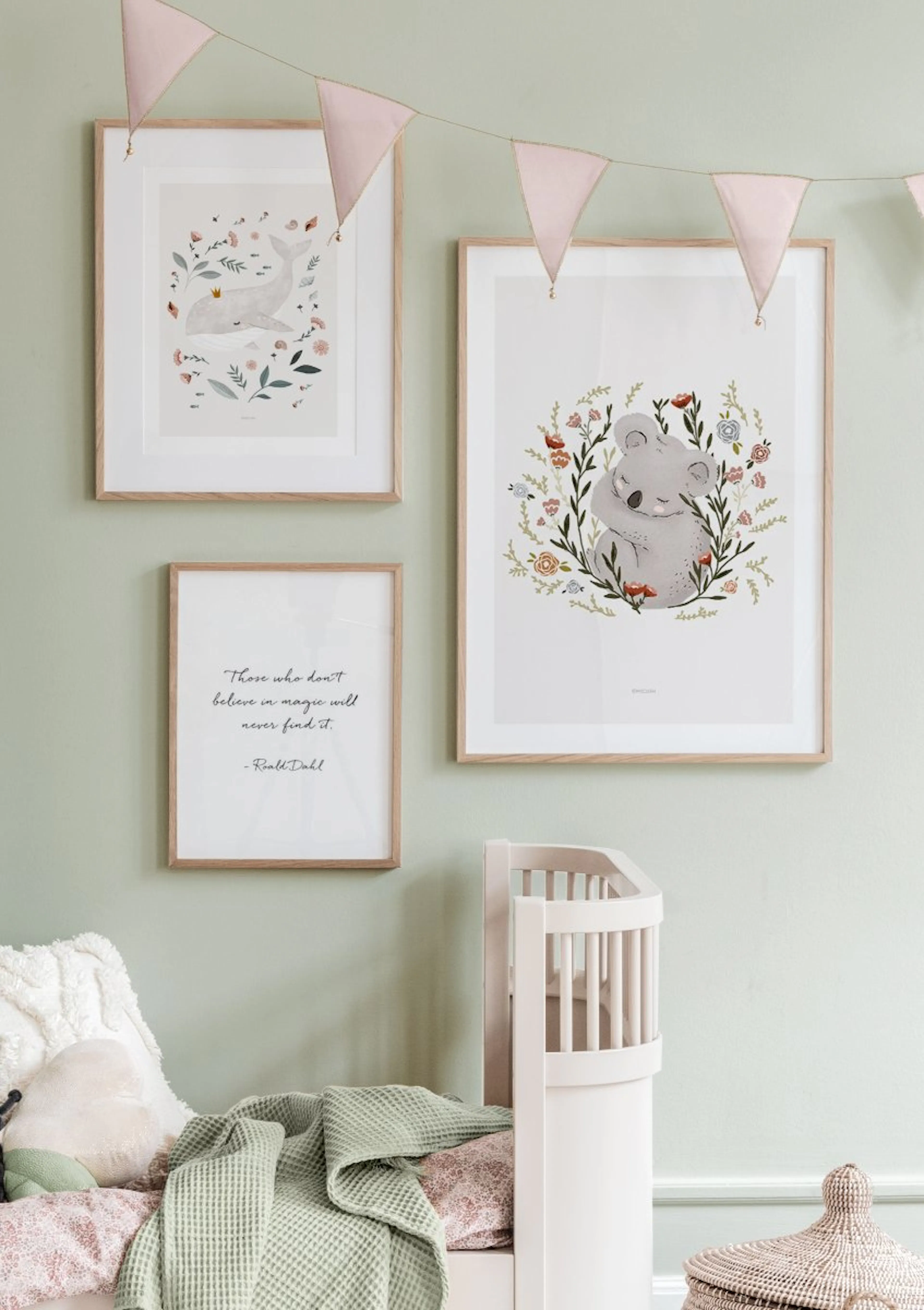 淡いグリーンの壁に飾られた、クジラ、コアラ、引用句の3枚のポスター。ベビーベッドとピンクのガーランドが手前に見える。