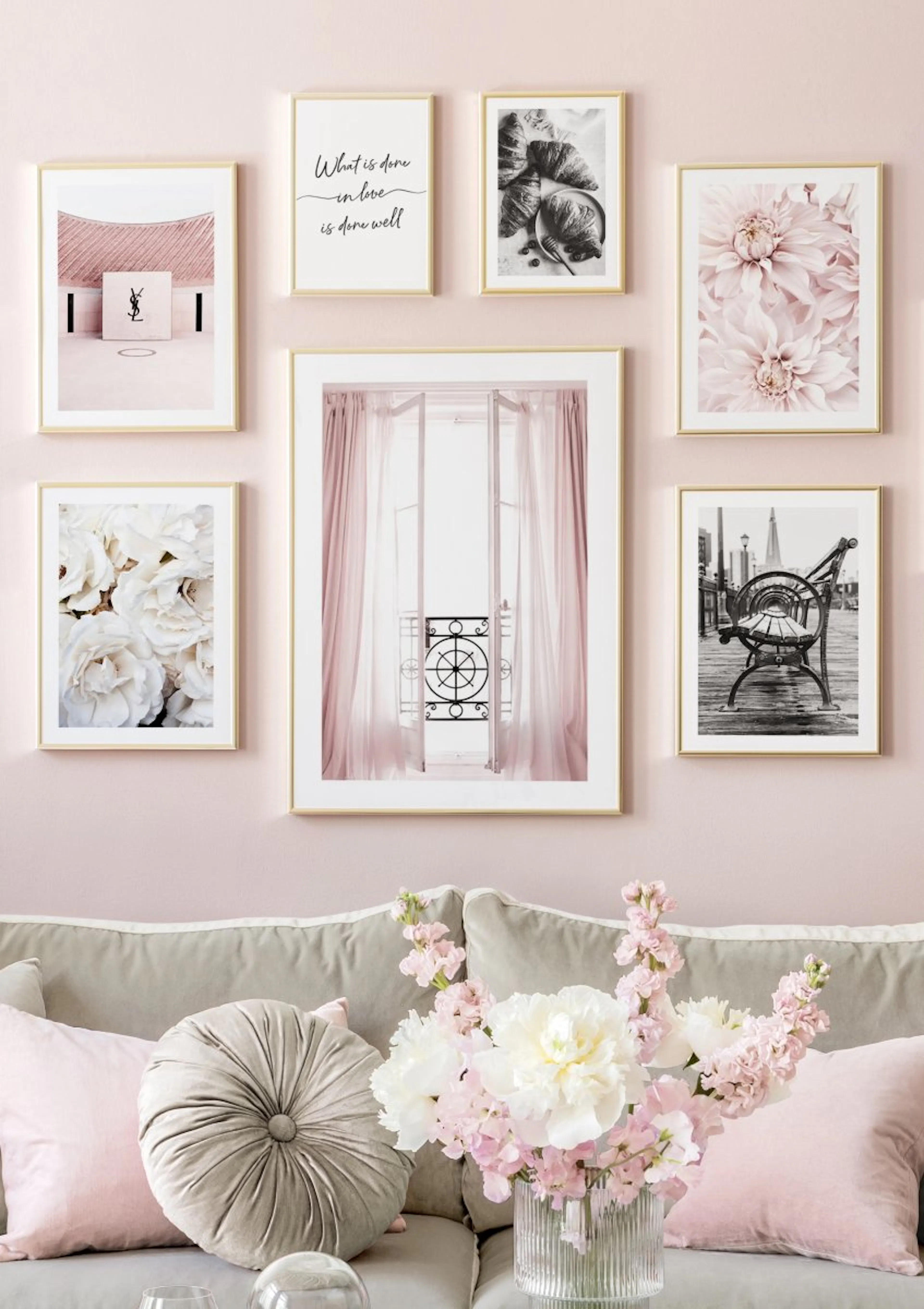 A gallery wall with seven posters on a pink wall above a grey sofa, featuring prints of white flowers, pink dahlias, a pink balc