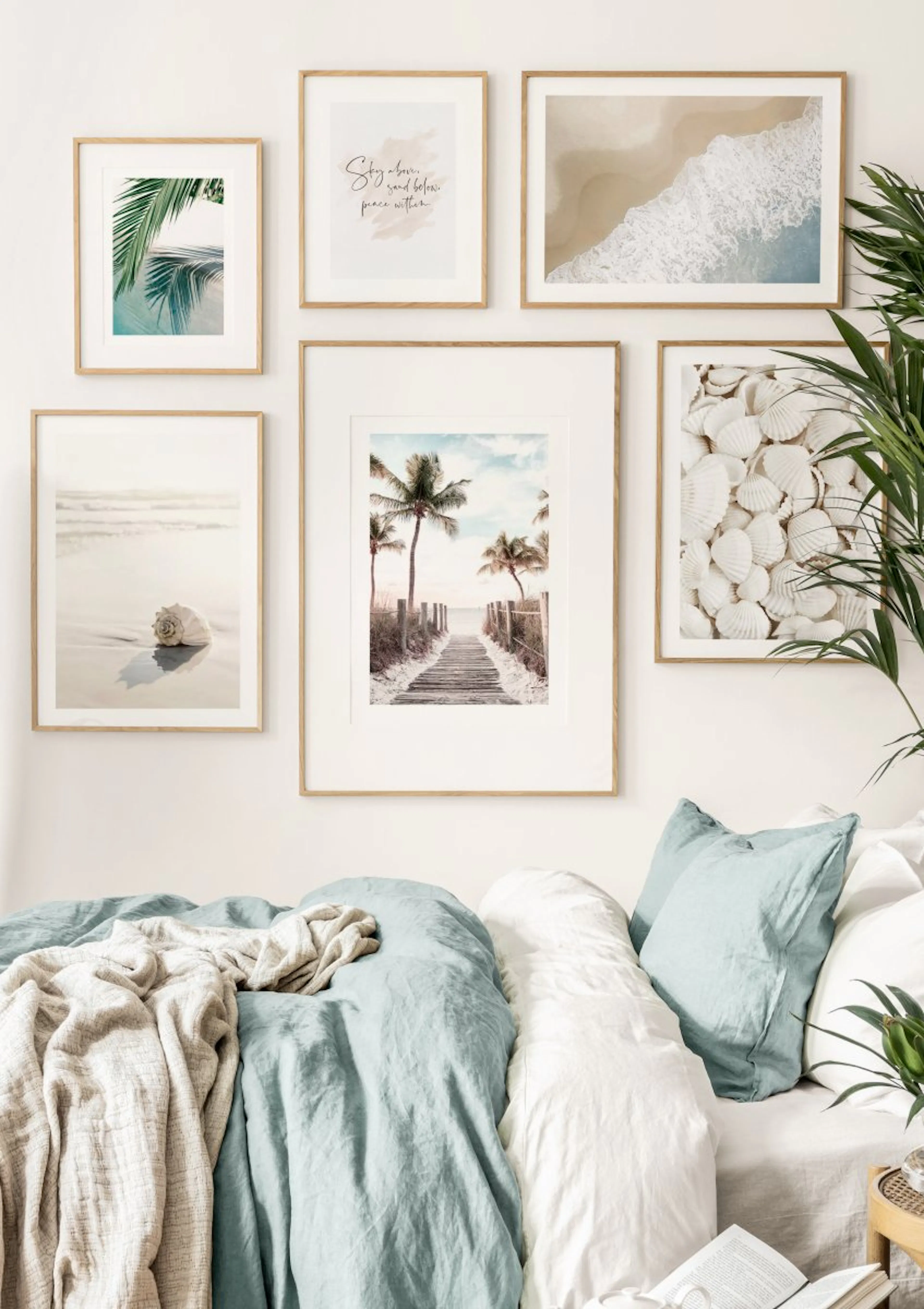 Eine Bilderwand mit sechs Postern von Strandszenen, Muscheln und Palmen über einem Bett mit blauer Bettwäsche in einem Schlafzim
