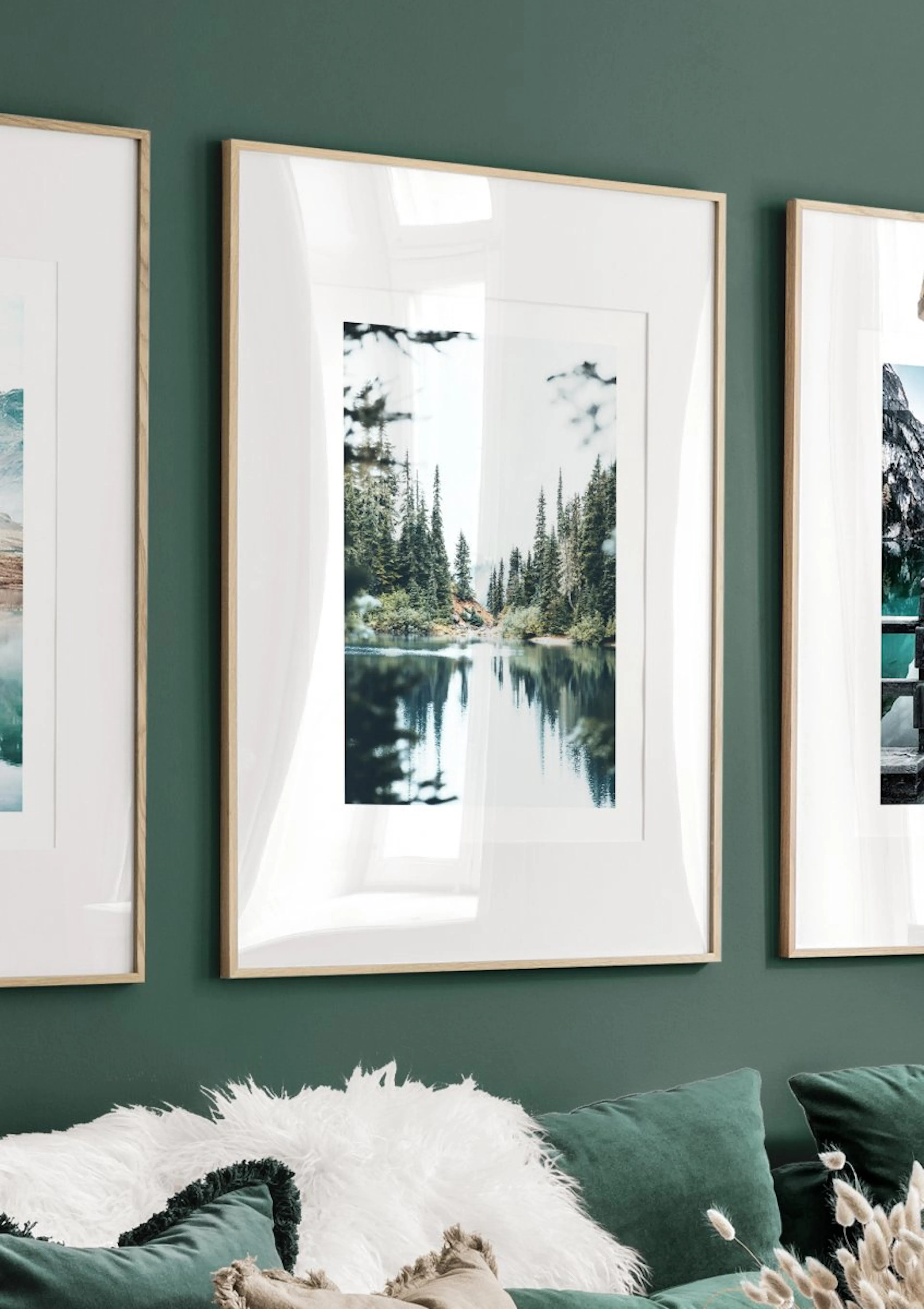 A poster depicting a serene lake reflecting pine trees and a distant shore, hanging on a dark green wall above a sofa.