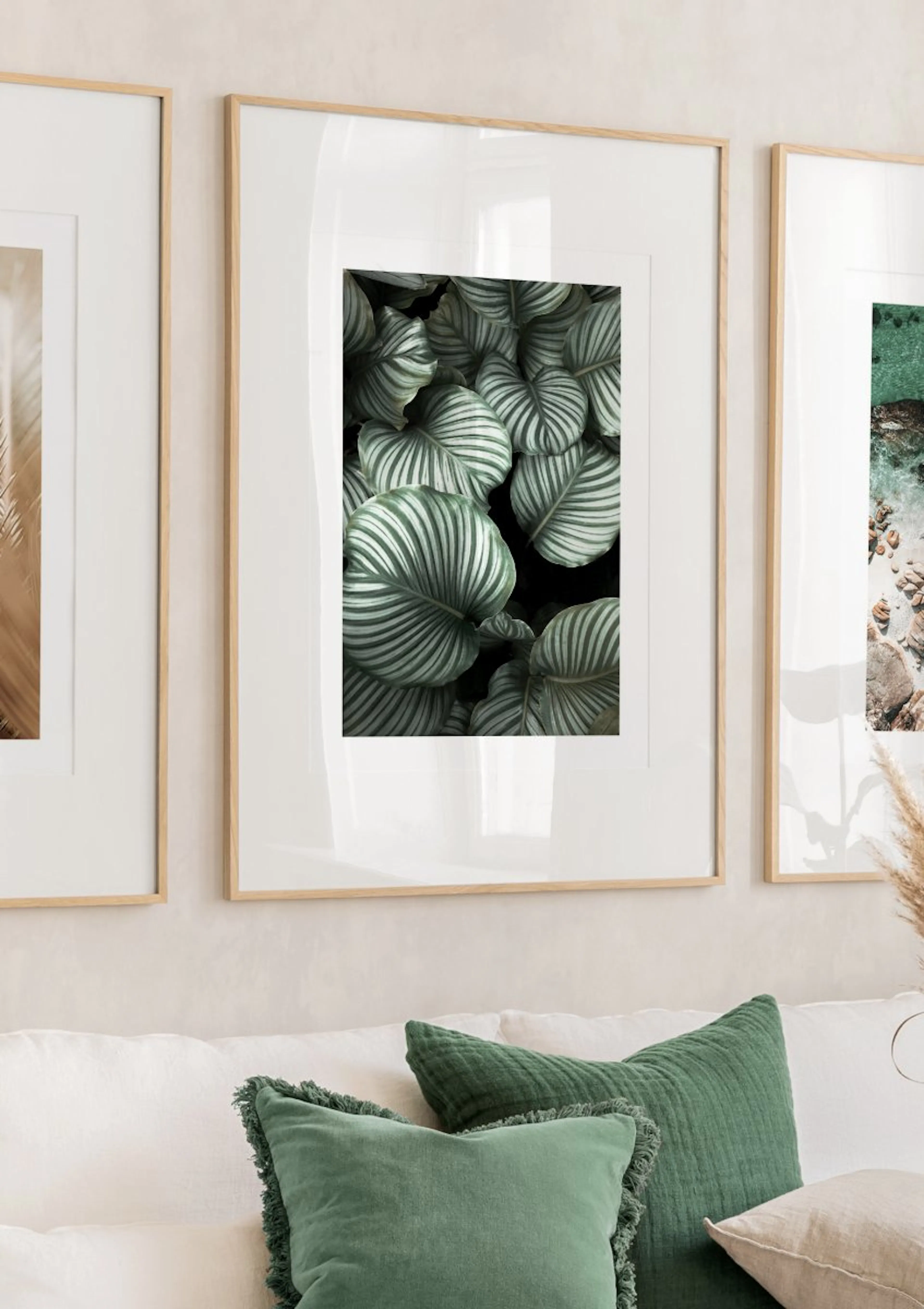 Print of lush green and white striped leaves on a dark background, displayed above a white sofa with green cushions.