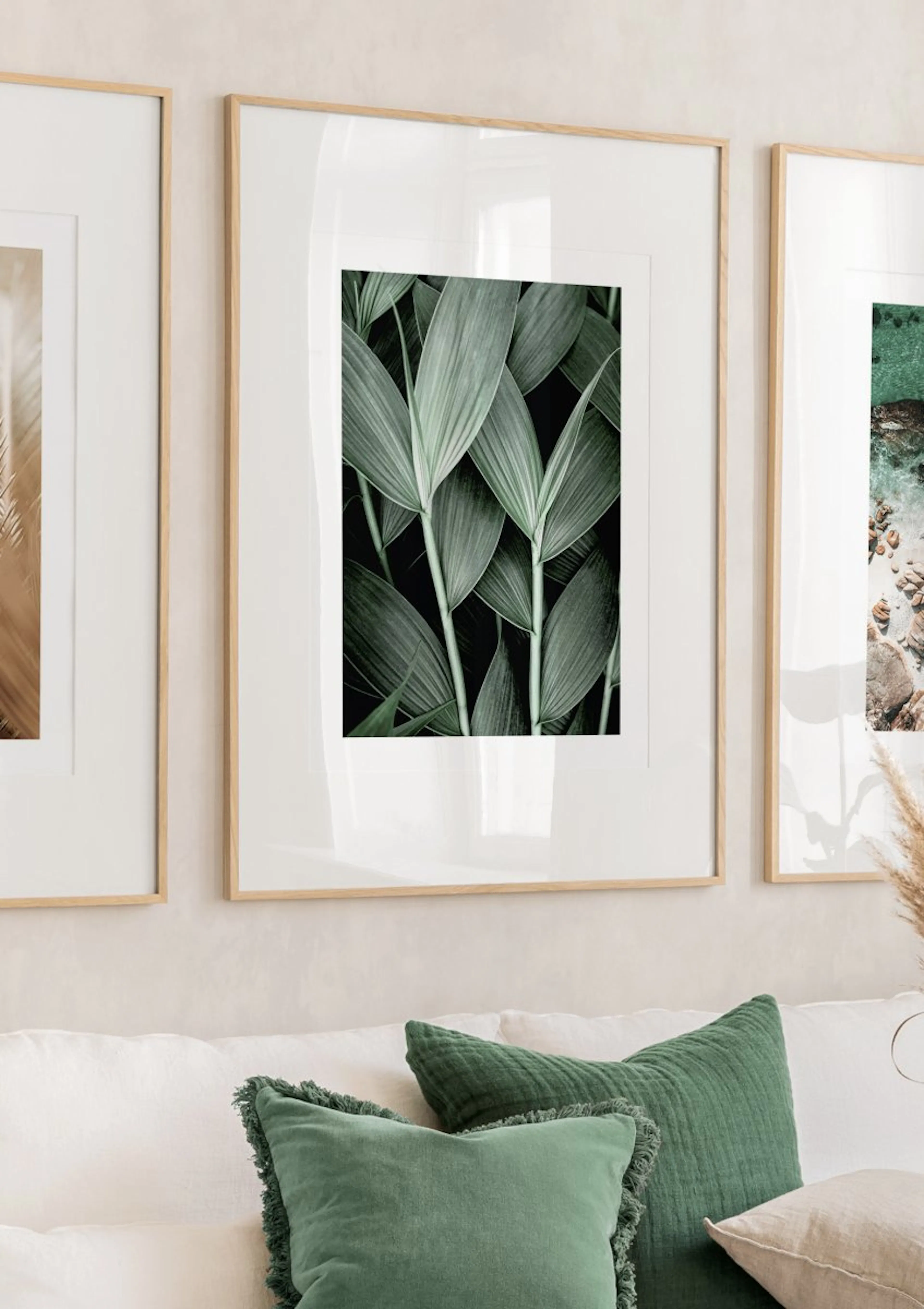 A poster featuring dark green palm leaves on a black background, displayed as part of a gallery wall above a white sofa with gre