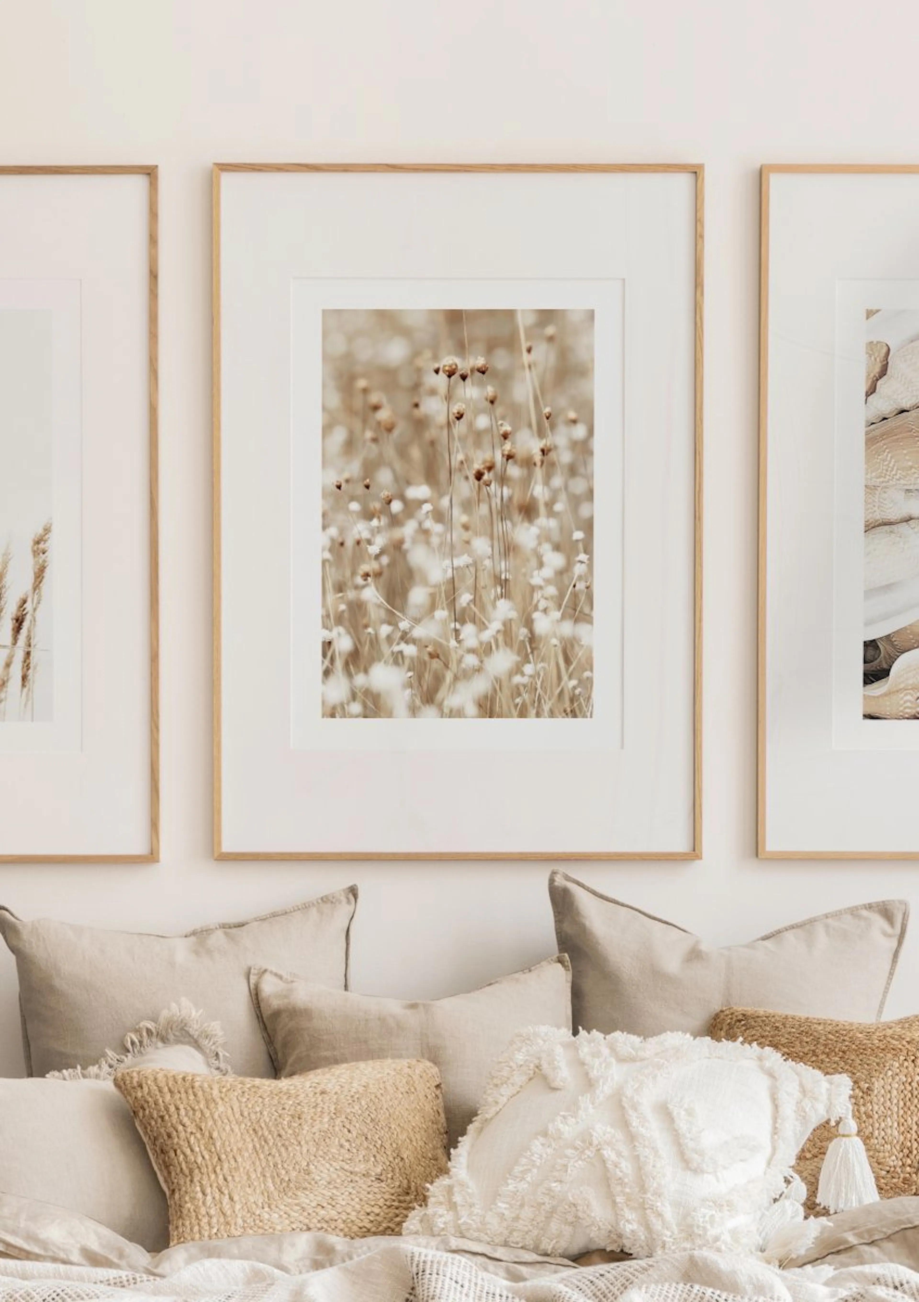 A poster of dried seed heads and white wildflowers in a field, displayed above a bed with neutral cushions.