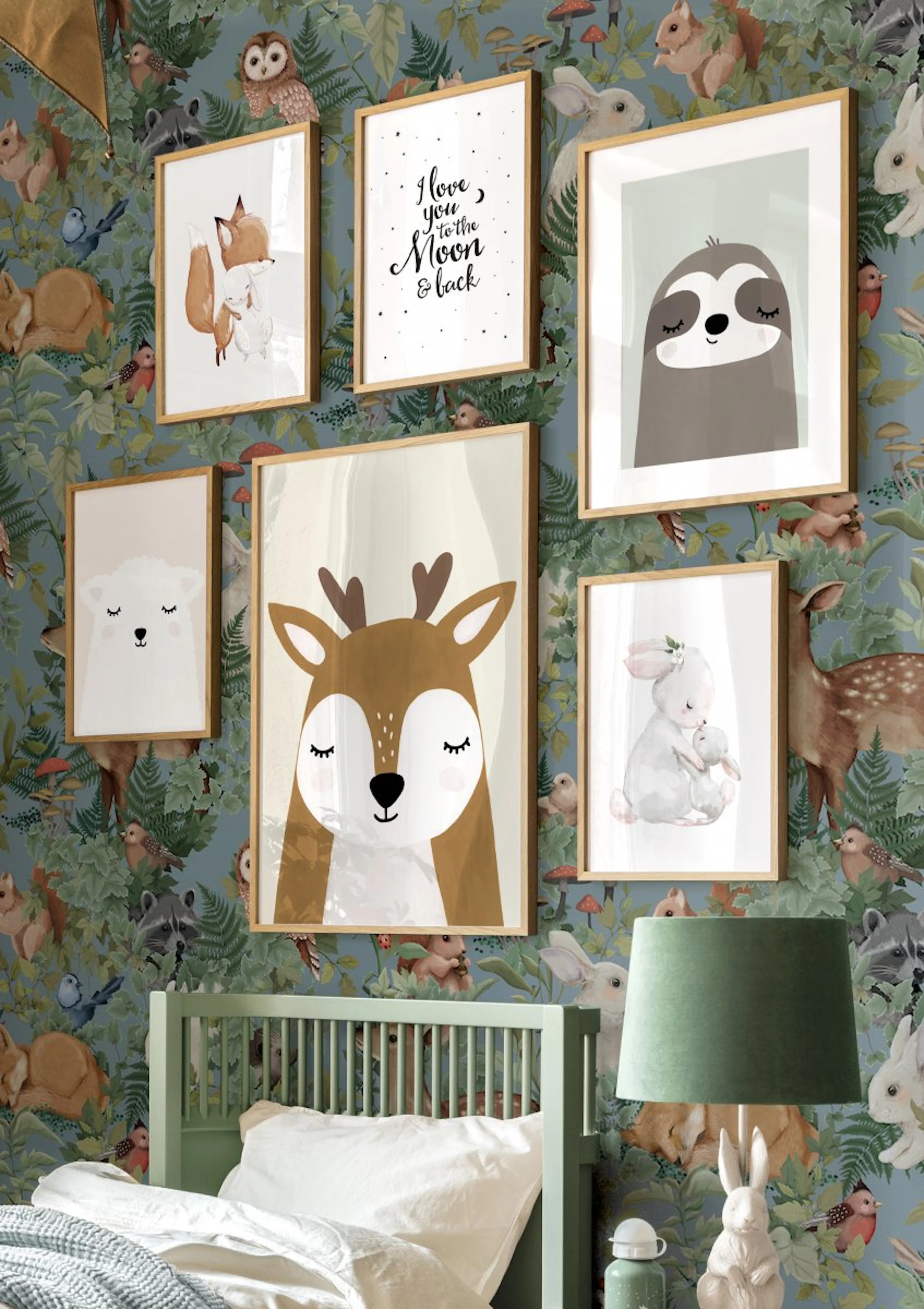 A gallery wall of six framed animal prints and a moon quote, hanging on a forest animal wallpaper above a green bed in a childs 