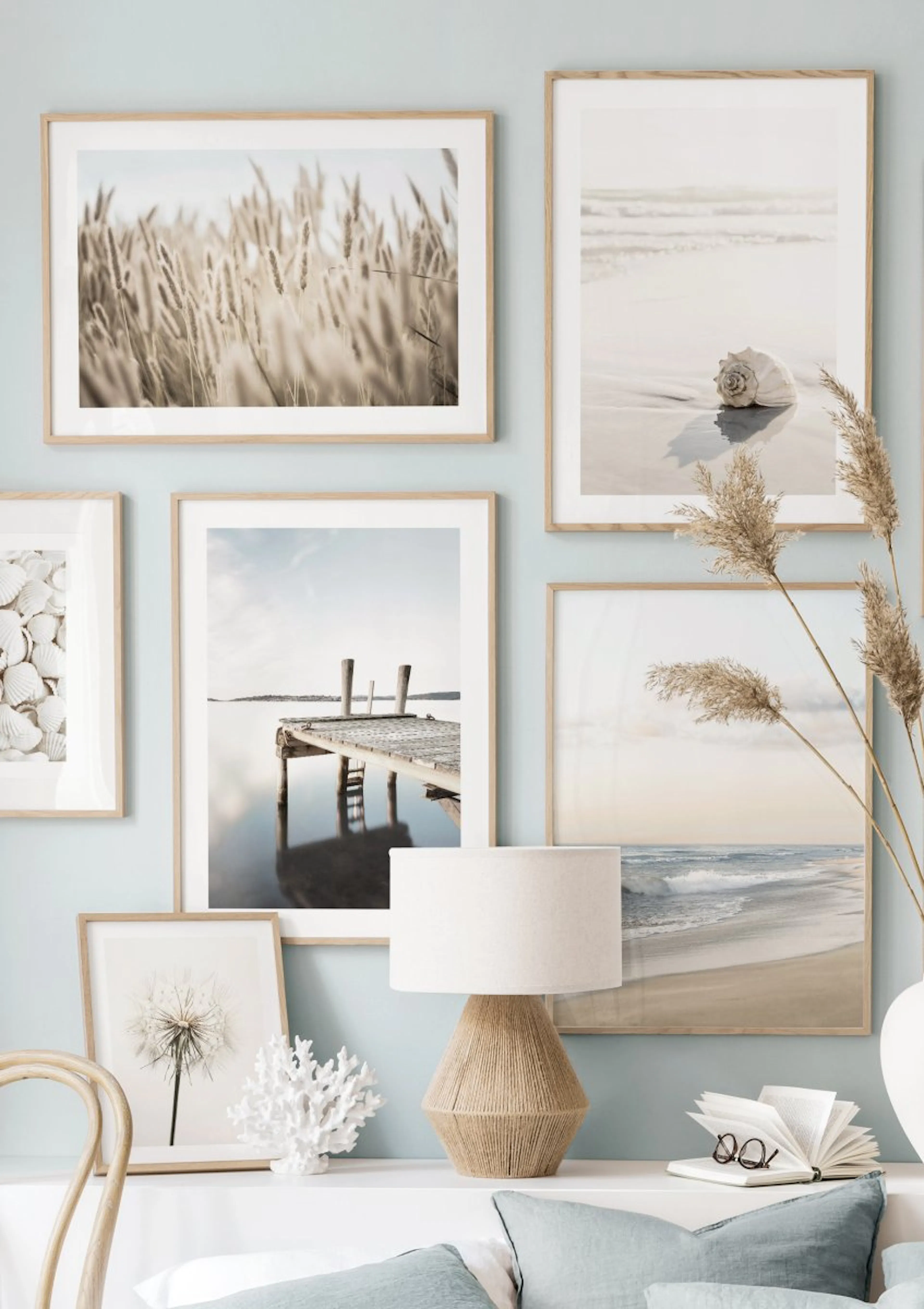 A gallery wall with six coastal posters including dry grass, a seashell, a pier, and ocean waves, displayed above a white consol
