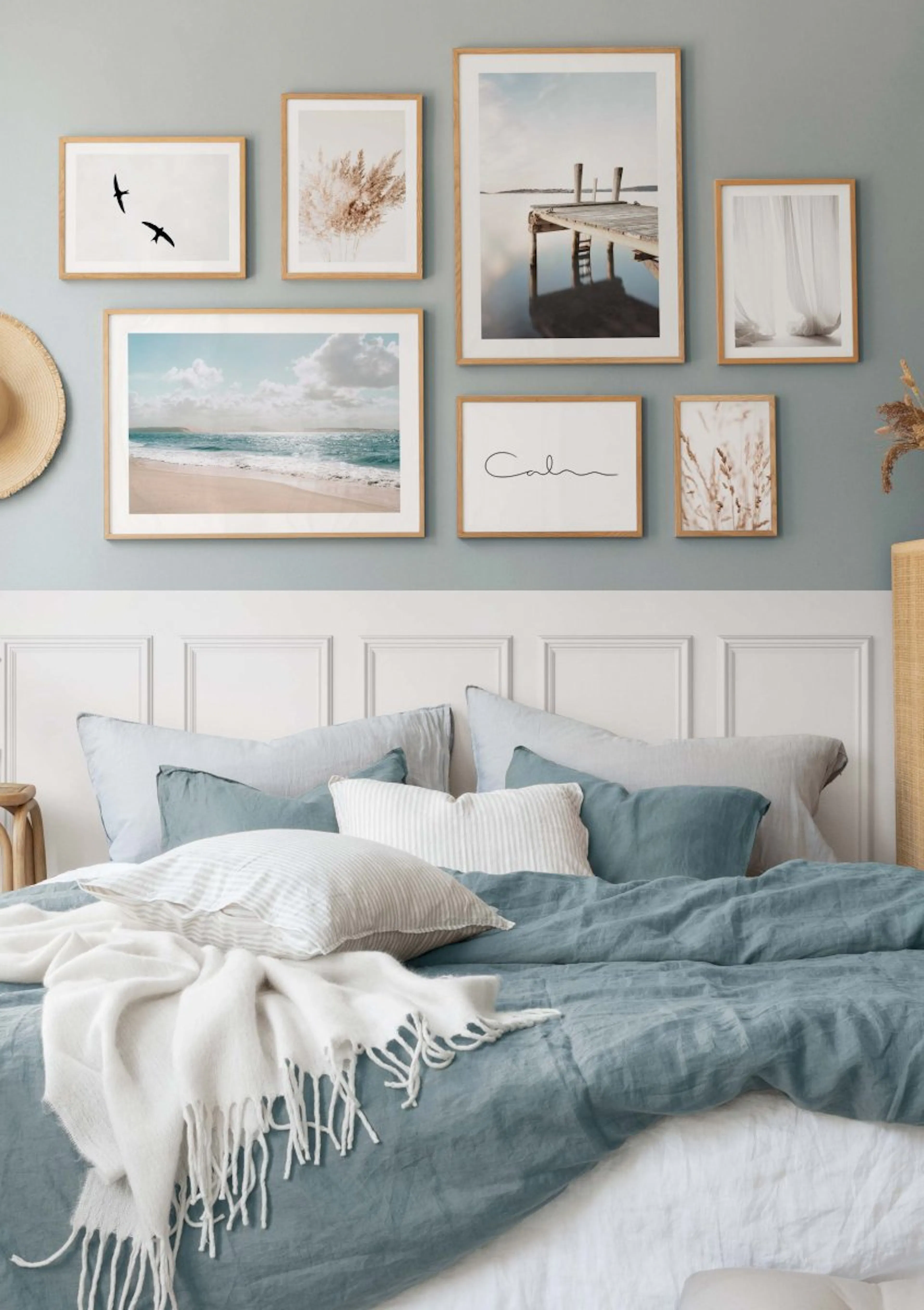 A gallery wall of six coastal and nature-themed posters above a bed with blue linen bedding in a bedroom.