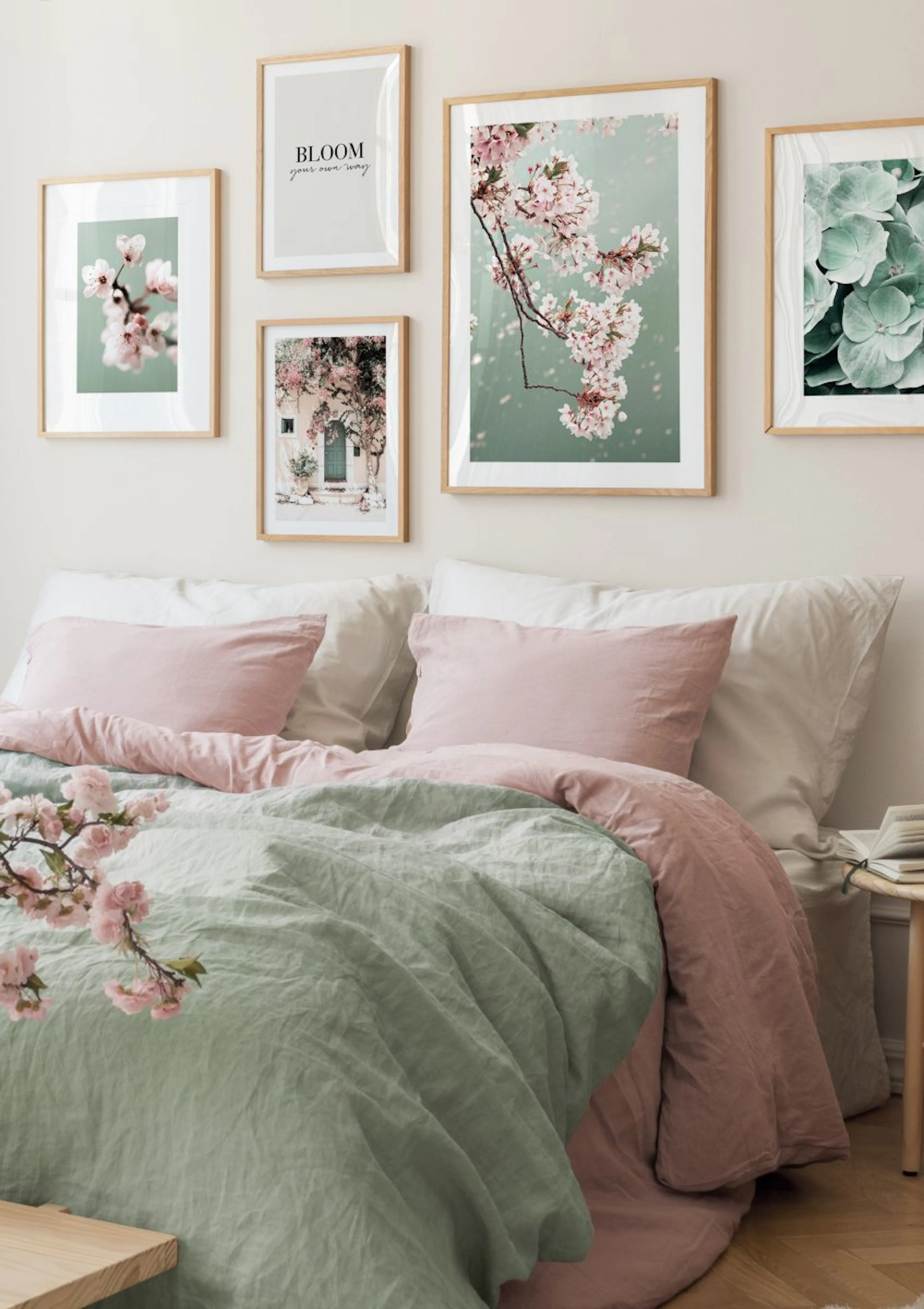 A gallery wall of botanical and inspirational posters above a bed with pink and sage green linen bedding.