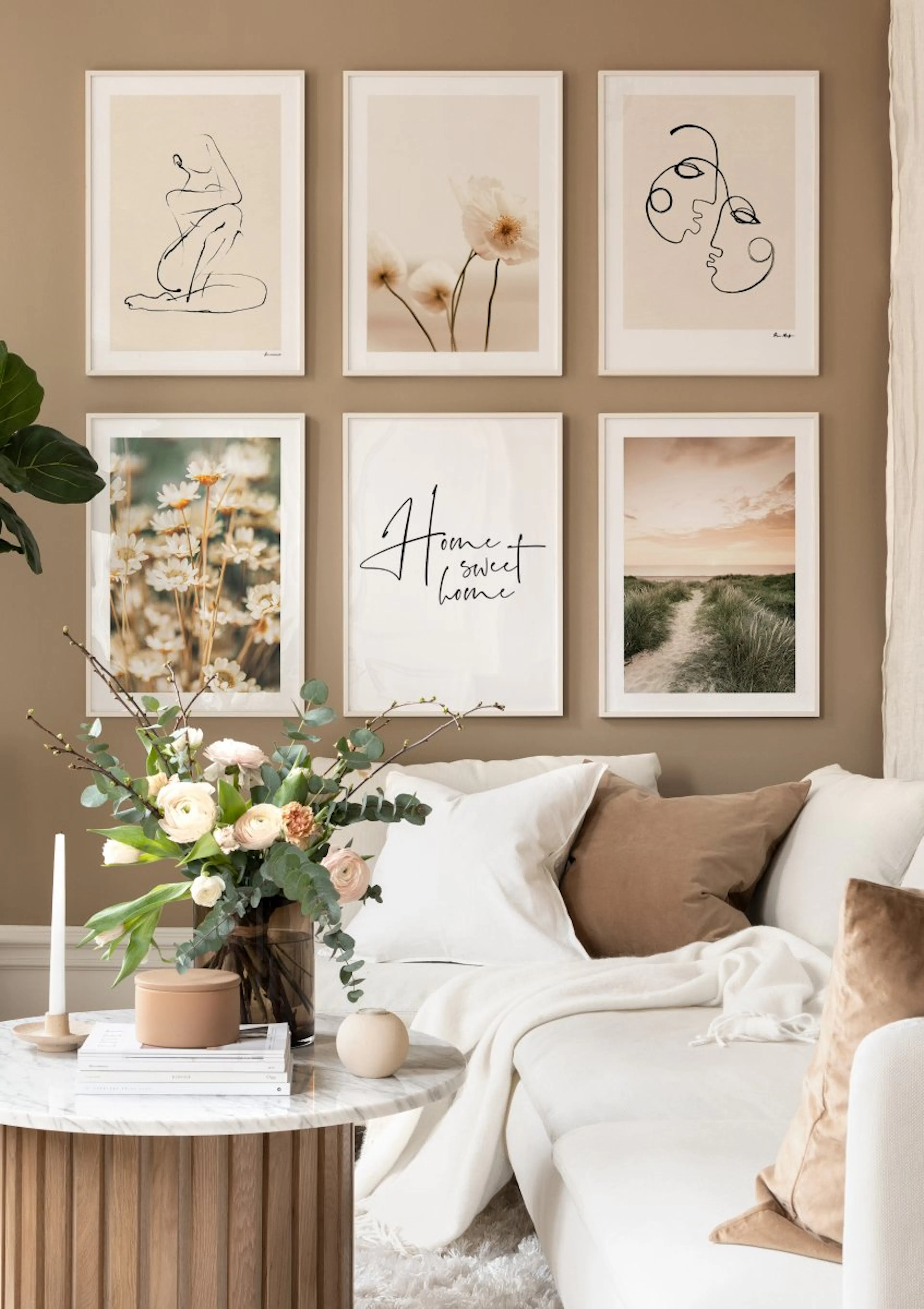 A gallery wall with six framed posters in a living room, featuring line art figures, flowers, text, and a beach path, above a so