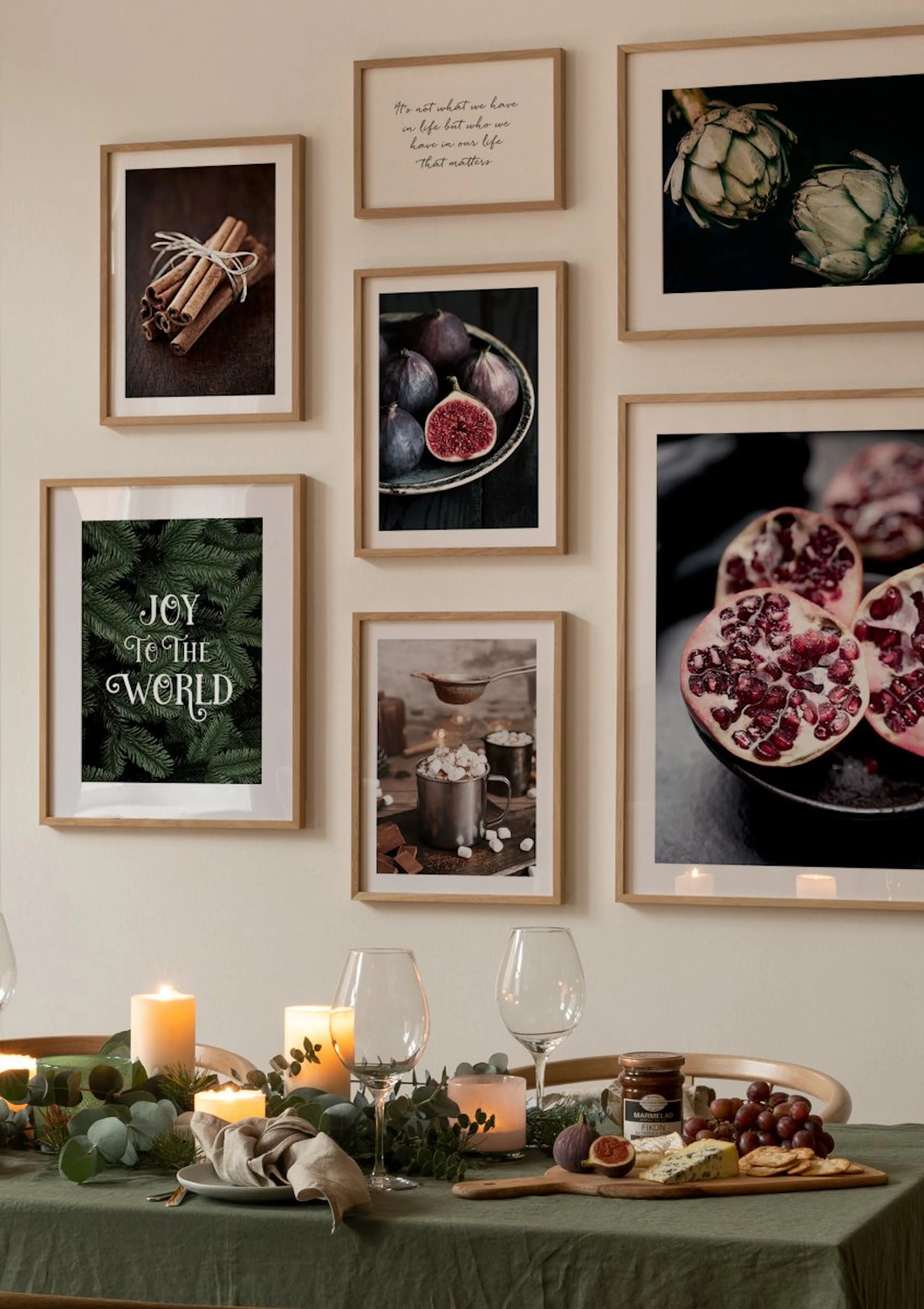 A gallery wall of posters with cinnamon, figs, pomegranates, hot cocoa, artichokes, a quote, and Joy to the World text, above a 