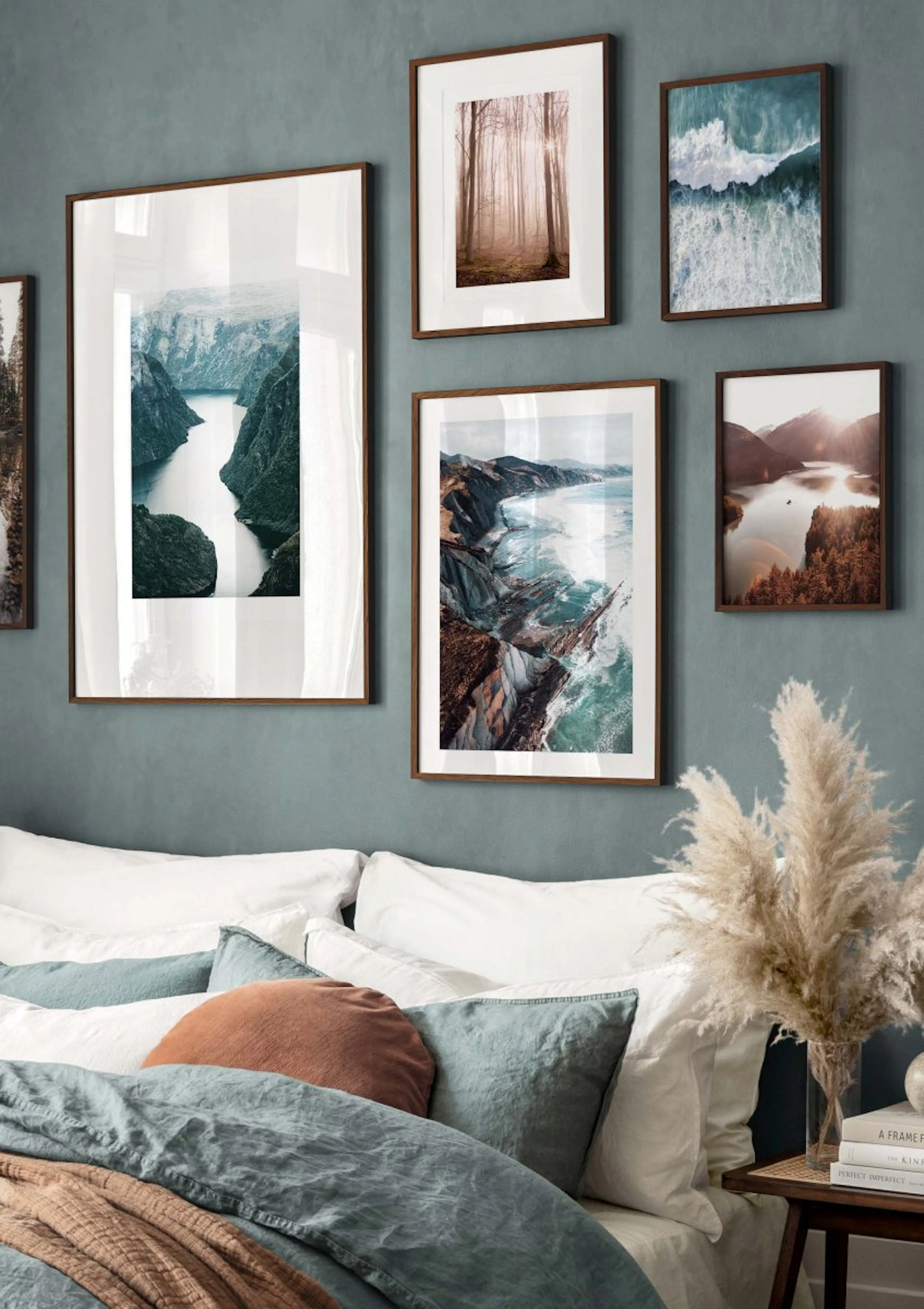 A gallery wall of nature posters, including a fjord, a forest, and a coastal landscape, hanging above a bed with blue and rust-c