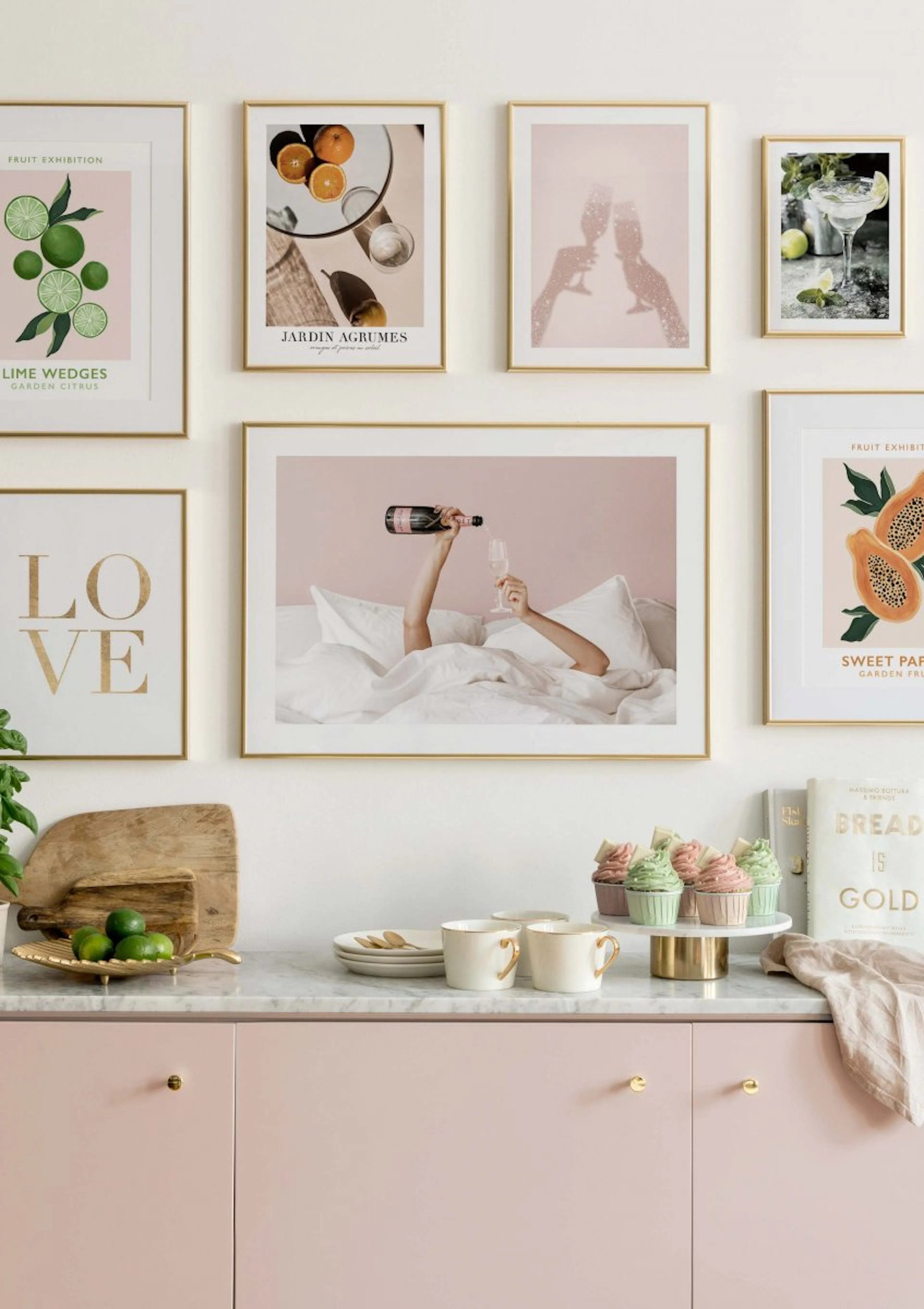 Eine Bilderwand mit Postern in Goldrahmen, hängend über einer rosa Küchenzeile mit Marmorplatte und Dekoration.